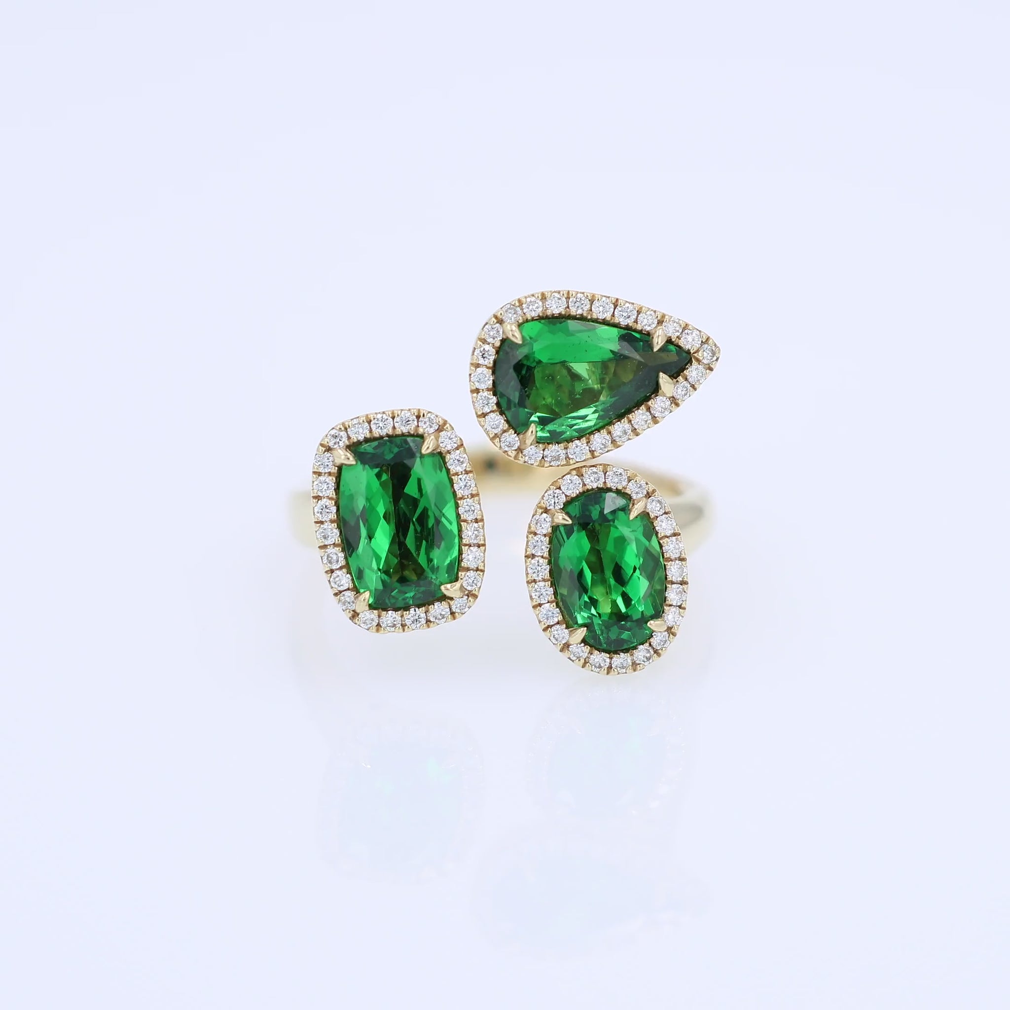 Gold ring with green tsavorite garnets and diamond halos on a white background