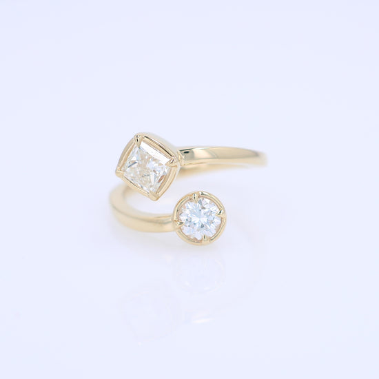 A yellow gold bypass ring featuring diamonds - a princess-cut and a round brilliant-cut diamond - on a clean white background.