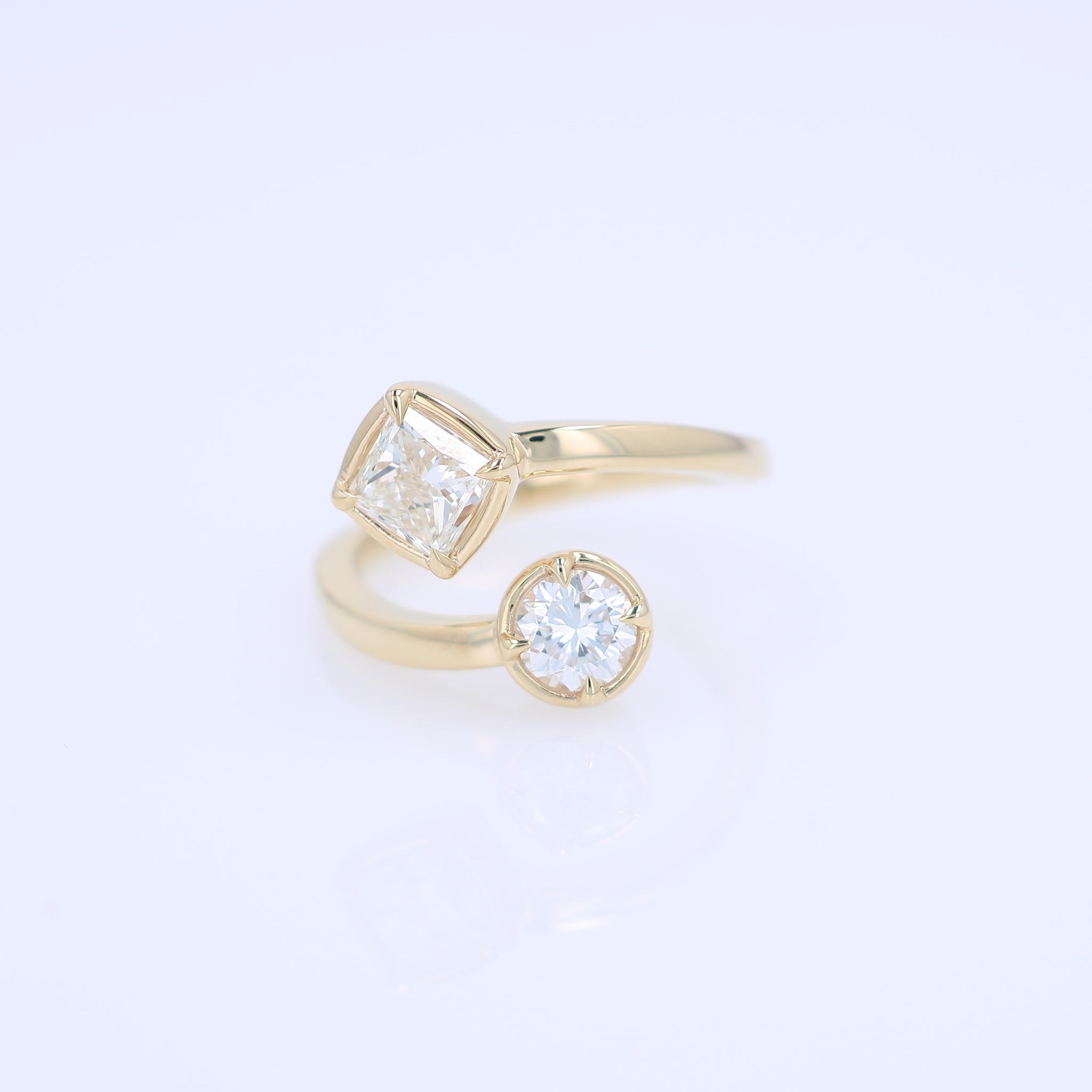 A yellow gold bypass ring featuring diamonds - a princess-cut and a round brilliant-cut diamond - on a clean white background.
