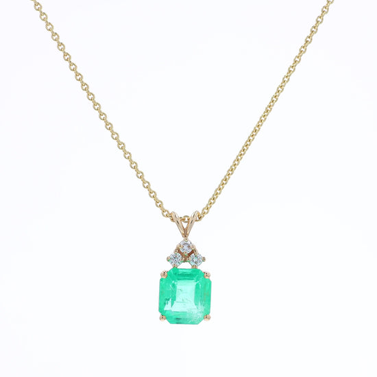 Yellow gold emerald cut emerald and diamond pendant necklace on a white background