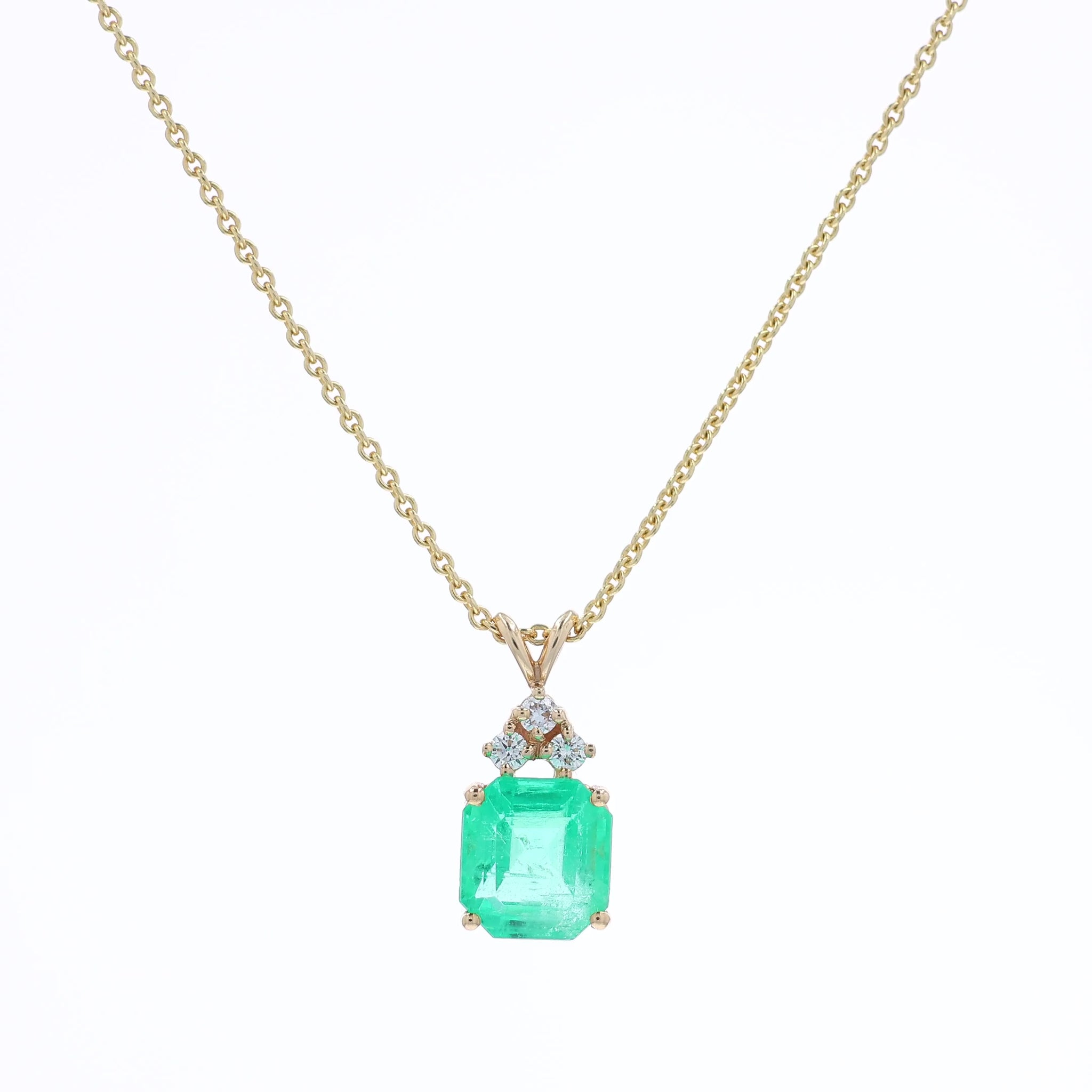 Yellow gold emerald cut emerald and diamond pendant necklace on a white background