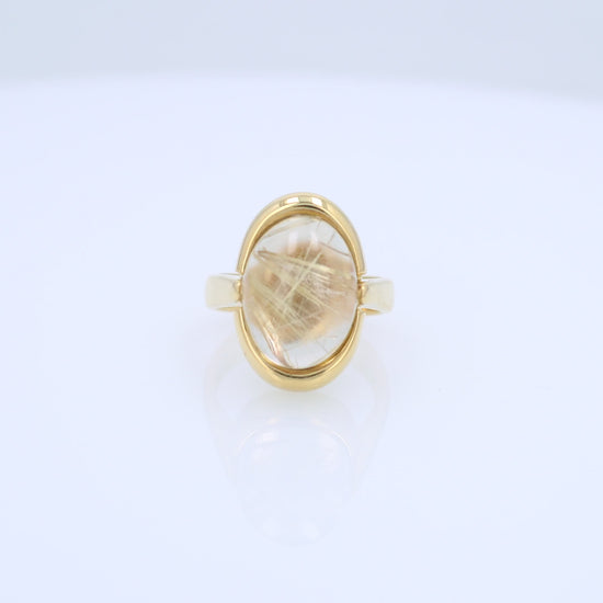 Yellow gold oval cabochon rutilated quartz ring on a white background