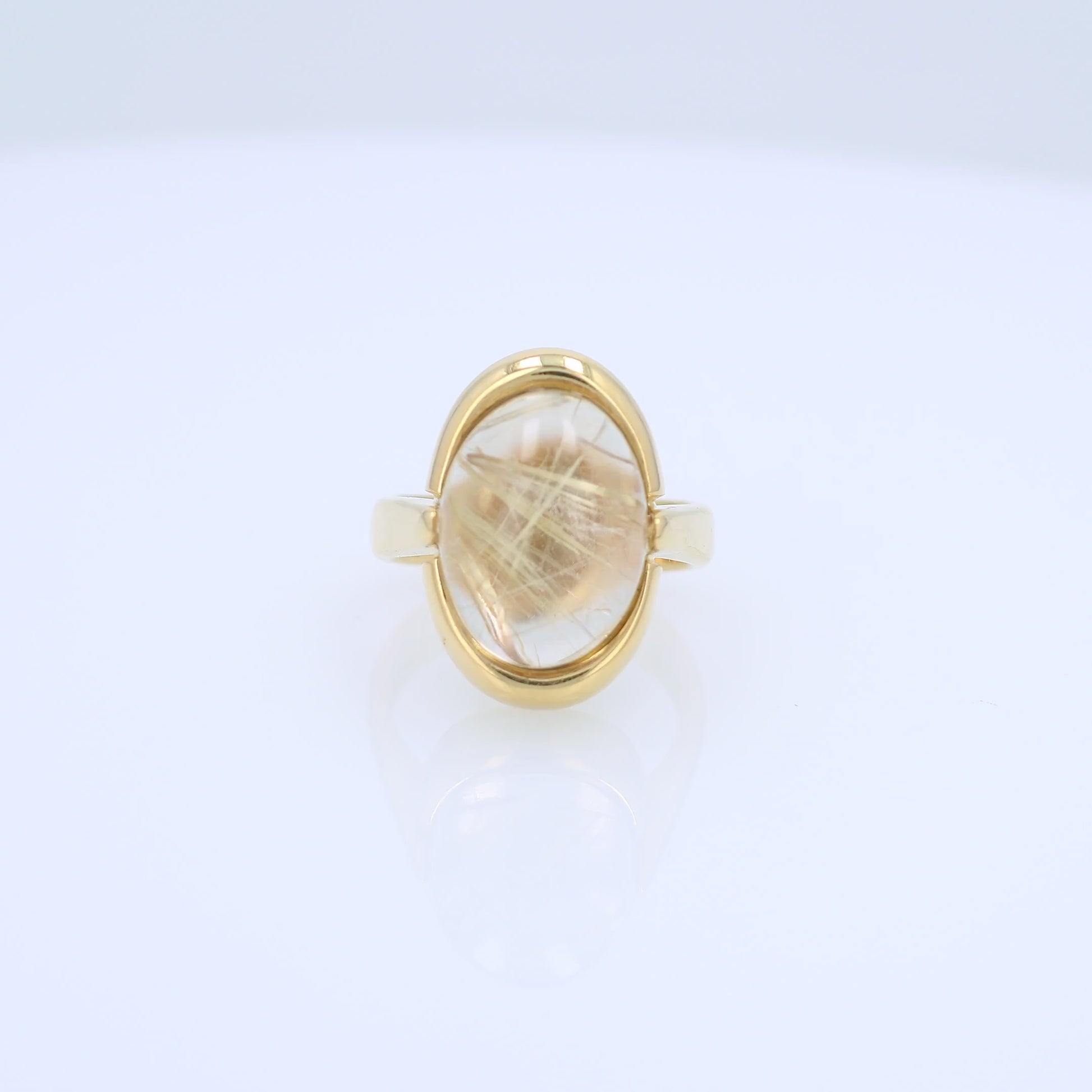 Yellow gold oval cabochon rutilated quartz ring on a white background