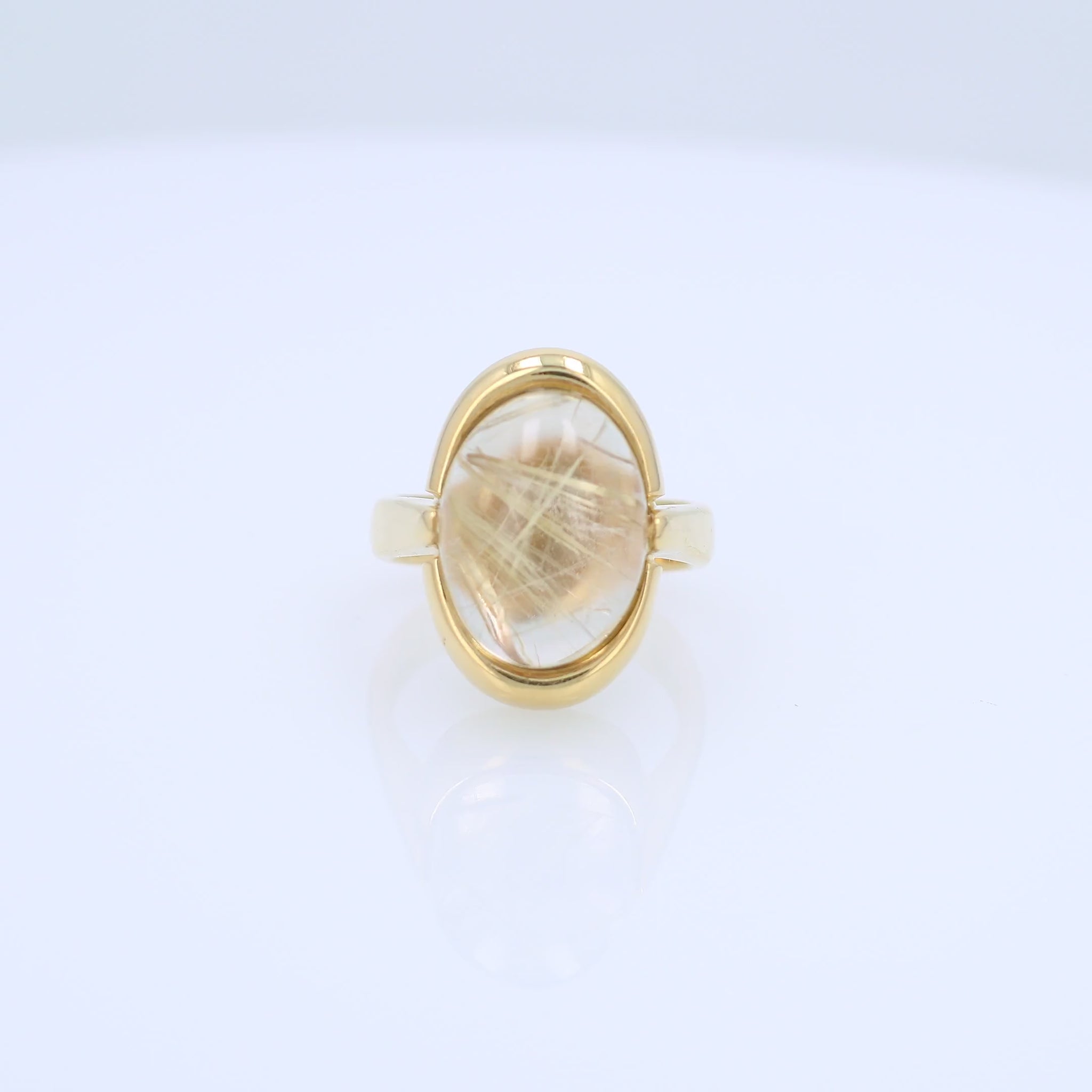 Yellow gold oval cabochon rutilated quartz ring on a white background
