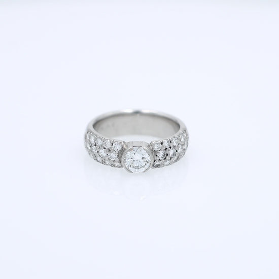 Platinum ring with a bezel set diamond center and pave diamonds on the shank on a white background