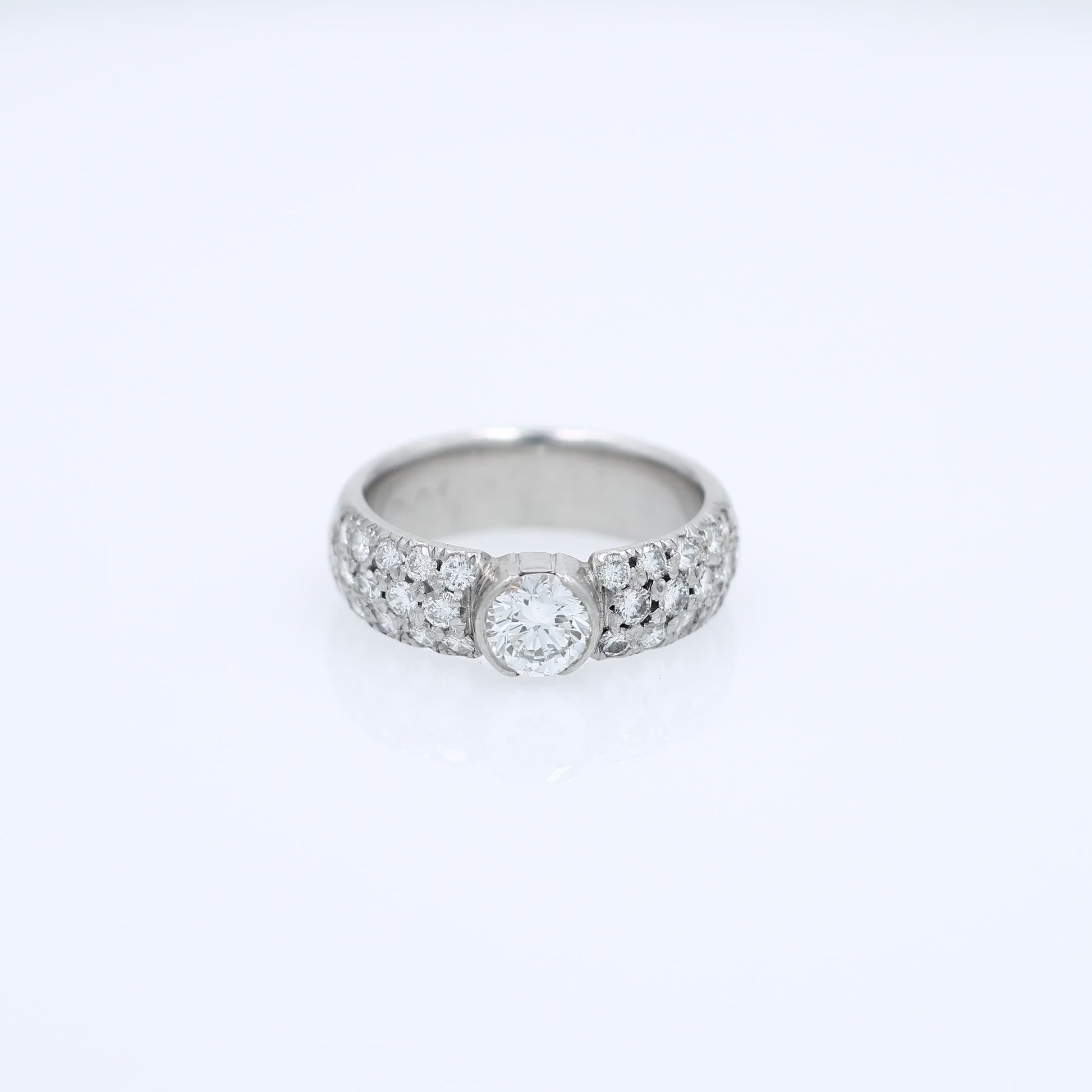 Platinum ring with a bezel set diamond center and pave diamonds on the shank on a white background