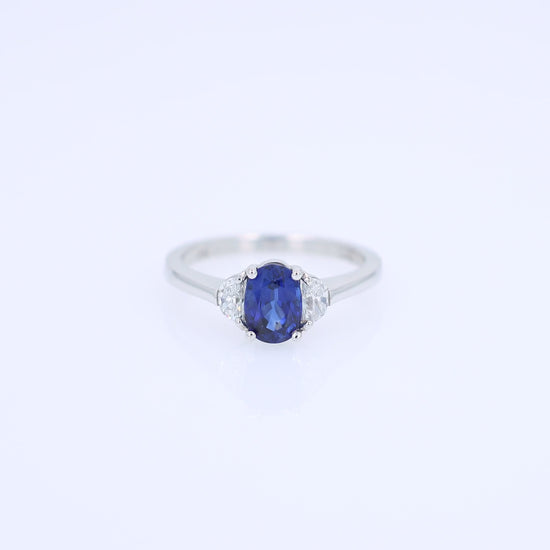Platinum ring with an oval blue sapphire center and half moon cut diamond sides on a white background