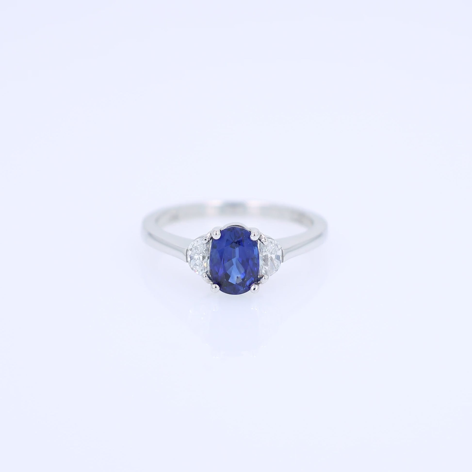 Platinum ring with an oval blue sapphire center and half moon cut diamond sides on a white background