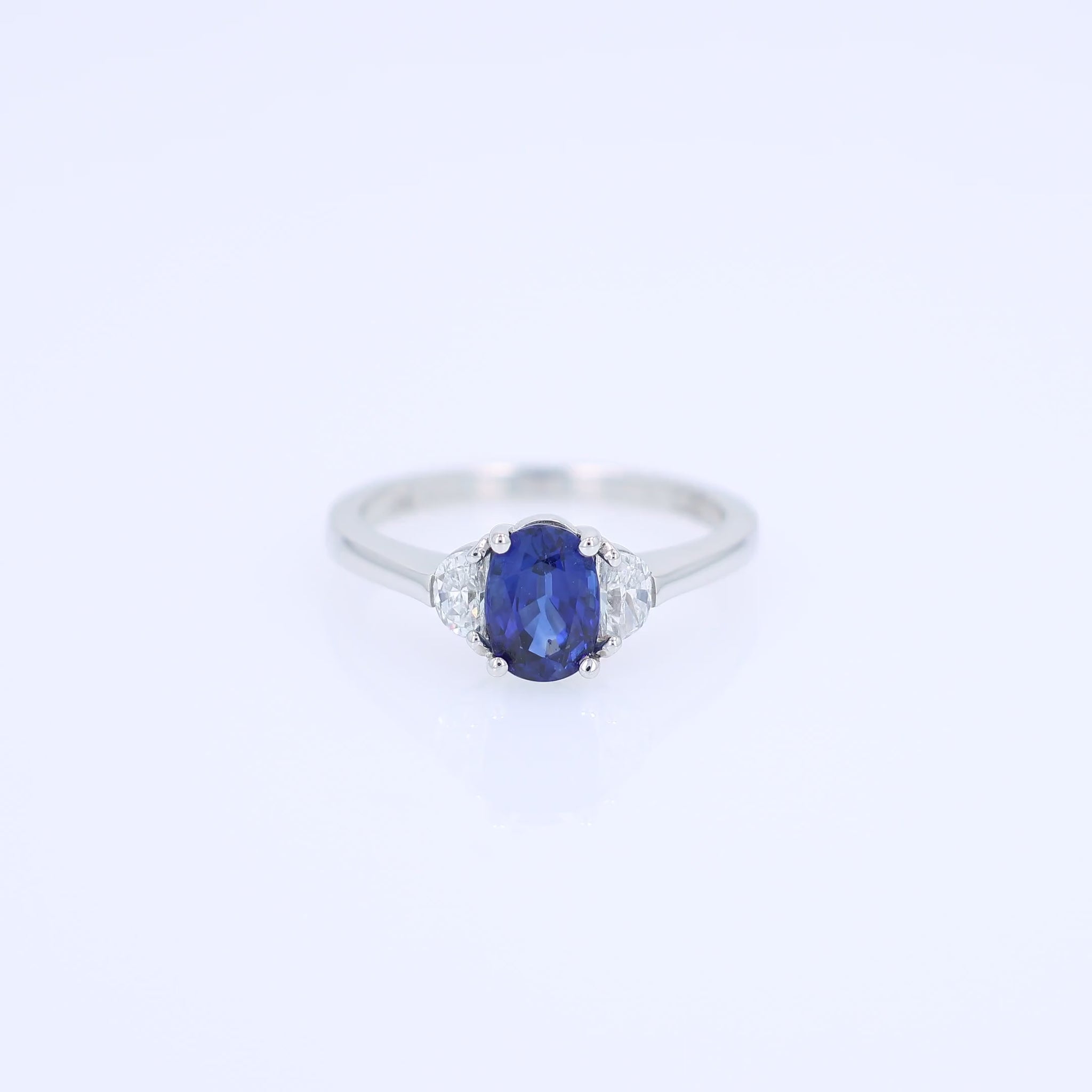 Platinum ring with an oval blue sapphire center and half moon cut diamond sides on a white background