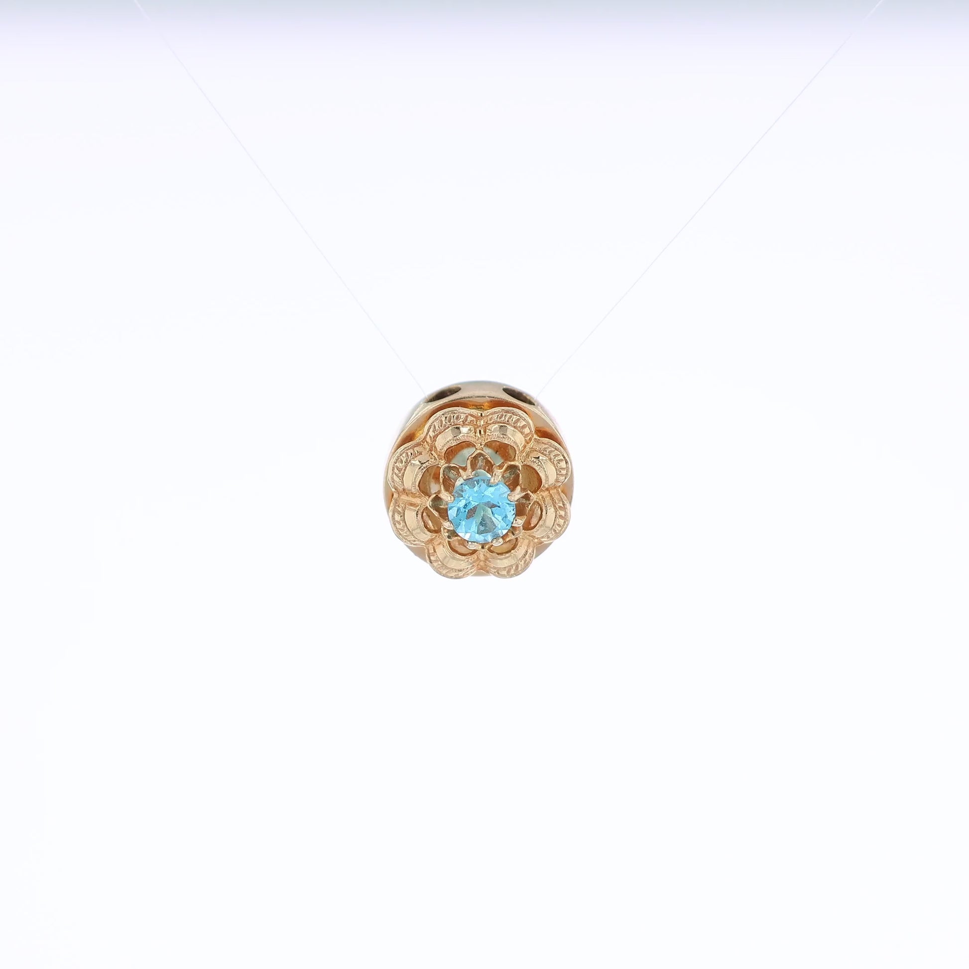 Yellow gold Victorian slide pendant with a blue topaz center and scalloped border on a white background