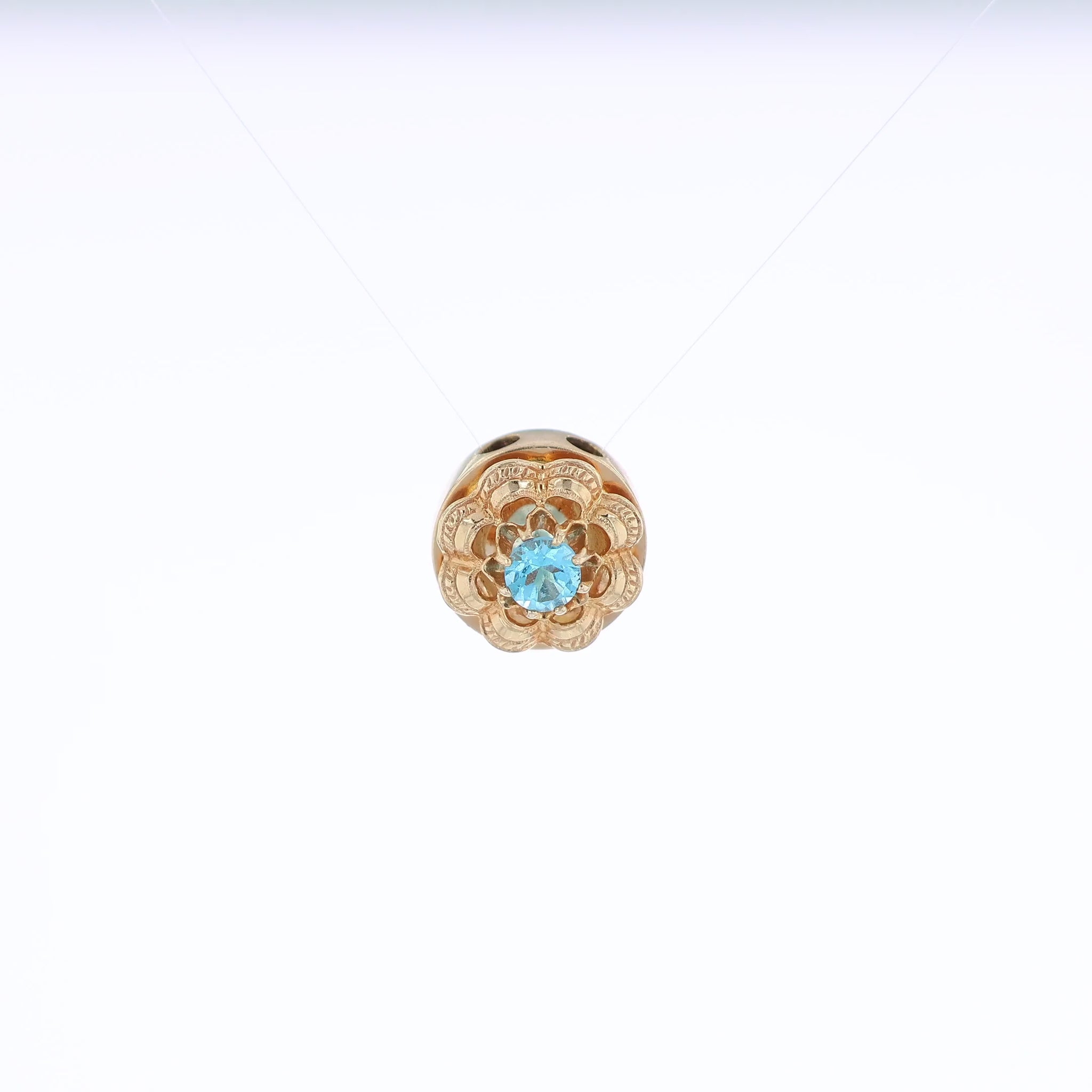 Yellow gold Victorian slide pendant with a blue topaz center and scalloped border on a white background