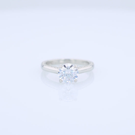 Platinum diamond solitaire engagement ring with engraved sides and a round cubic zirconia center on a white background