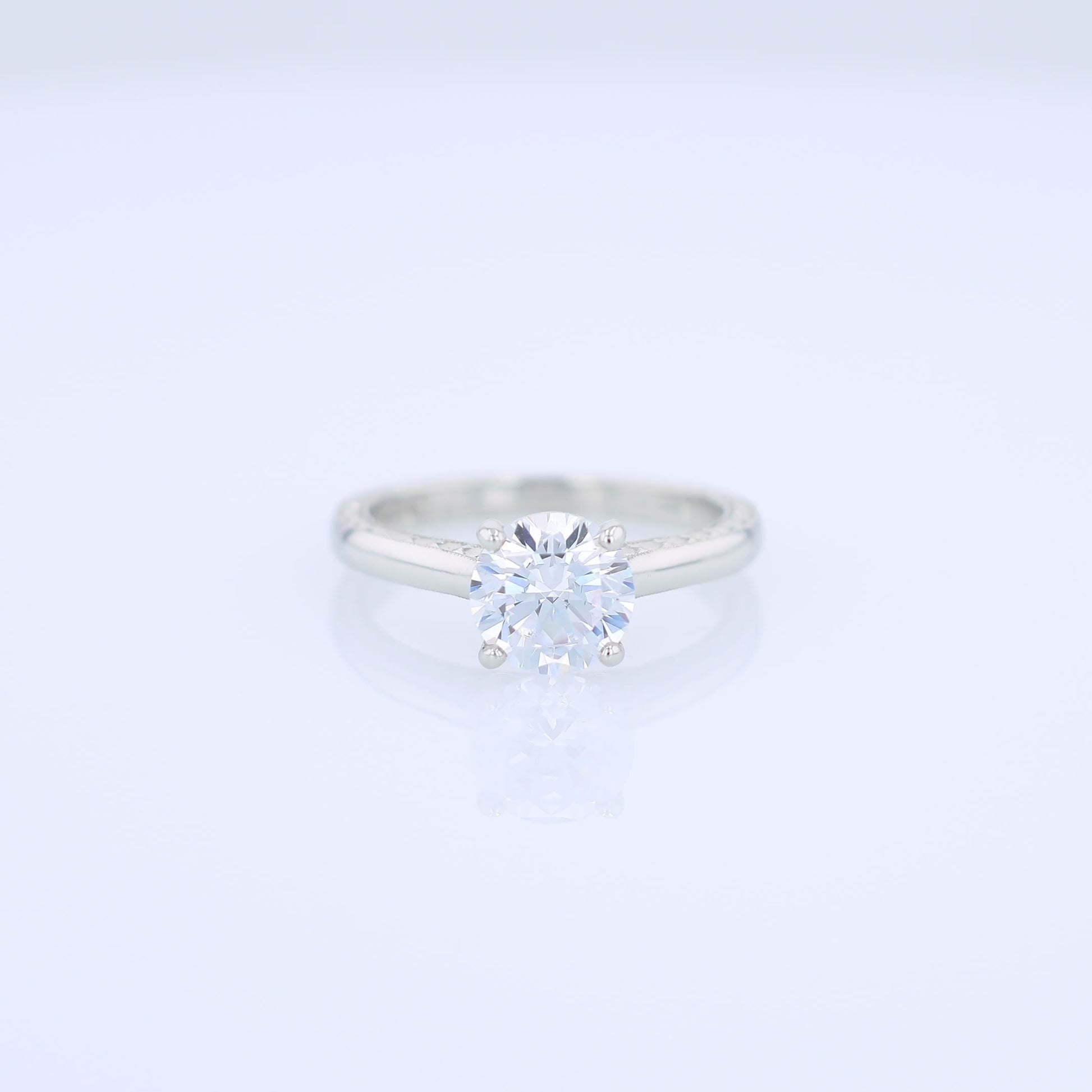 Platinum diamond solitaire engagement ring with engraved sides and a round cubic zirconia center on a white background