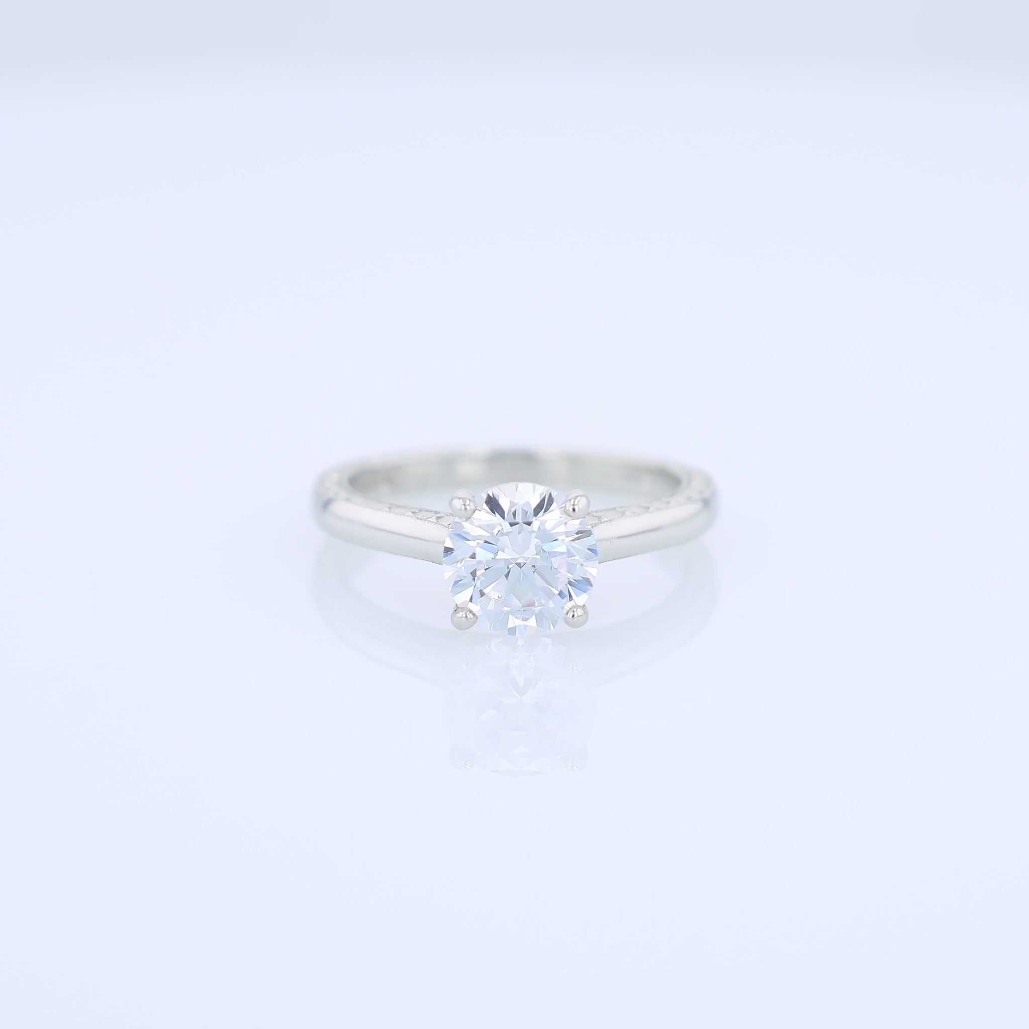 Platinum diamond solitaire engagement ring with engraved sides and a round cubic zirconia center on a white background