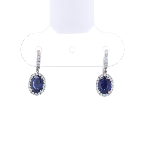 Pair of white gold diamond halo drop earrings with oval blue sapphire centers on a white background