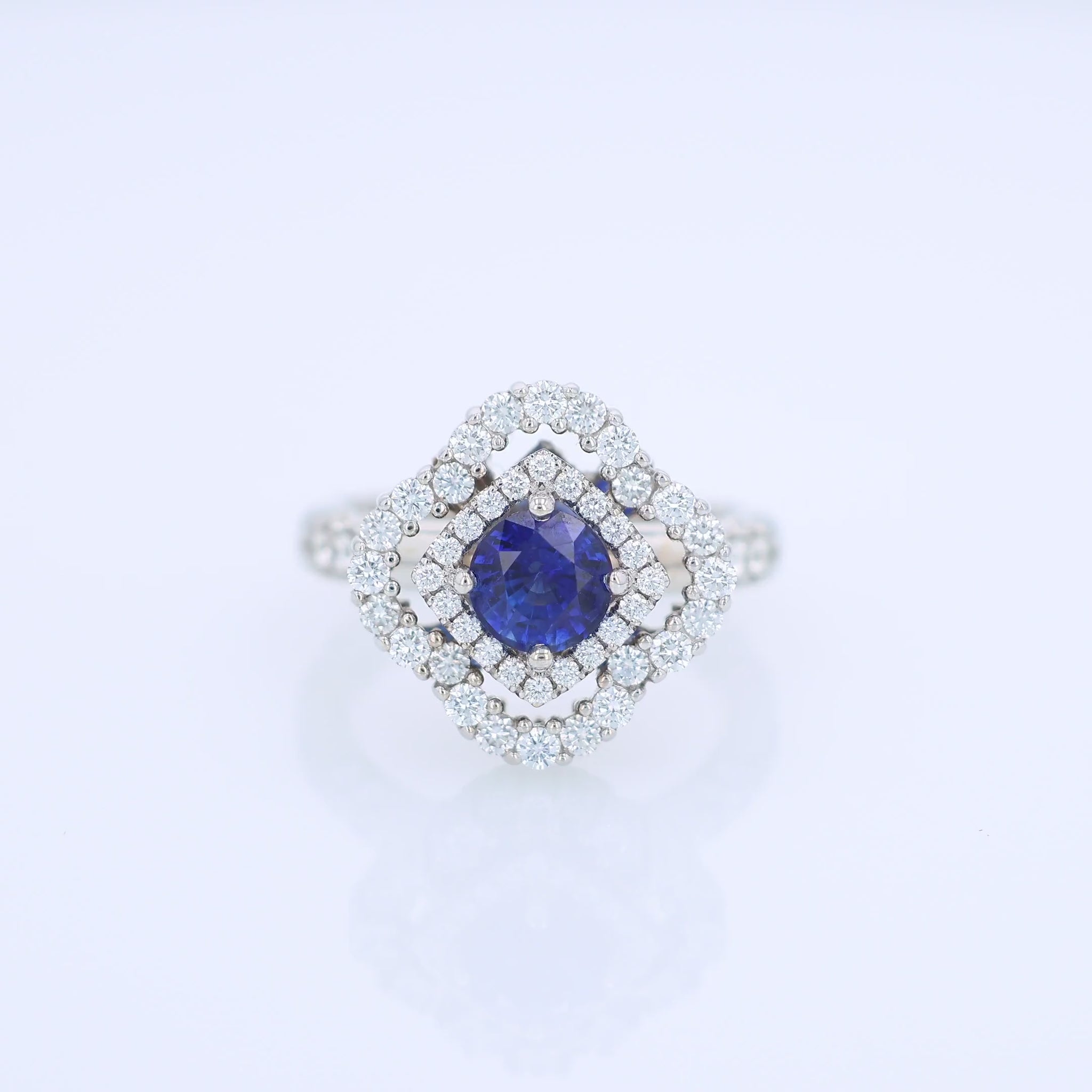 White gold diamond double halo ring with a blue sapphire center stone on a white background