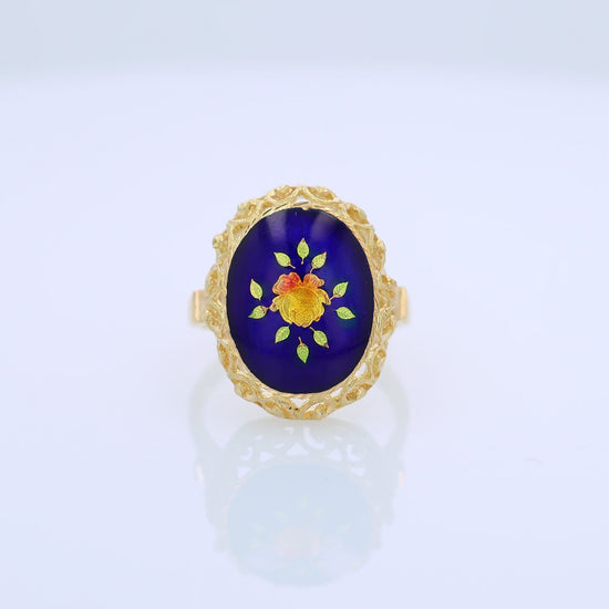 360 degree video of a yellow gold ring with a blue, orange and green flower design enamel center on a white background