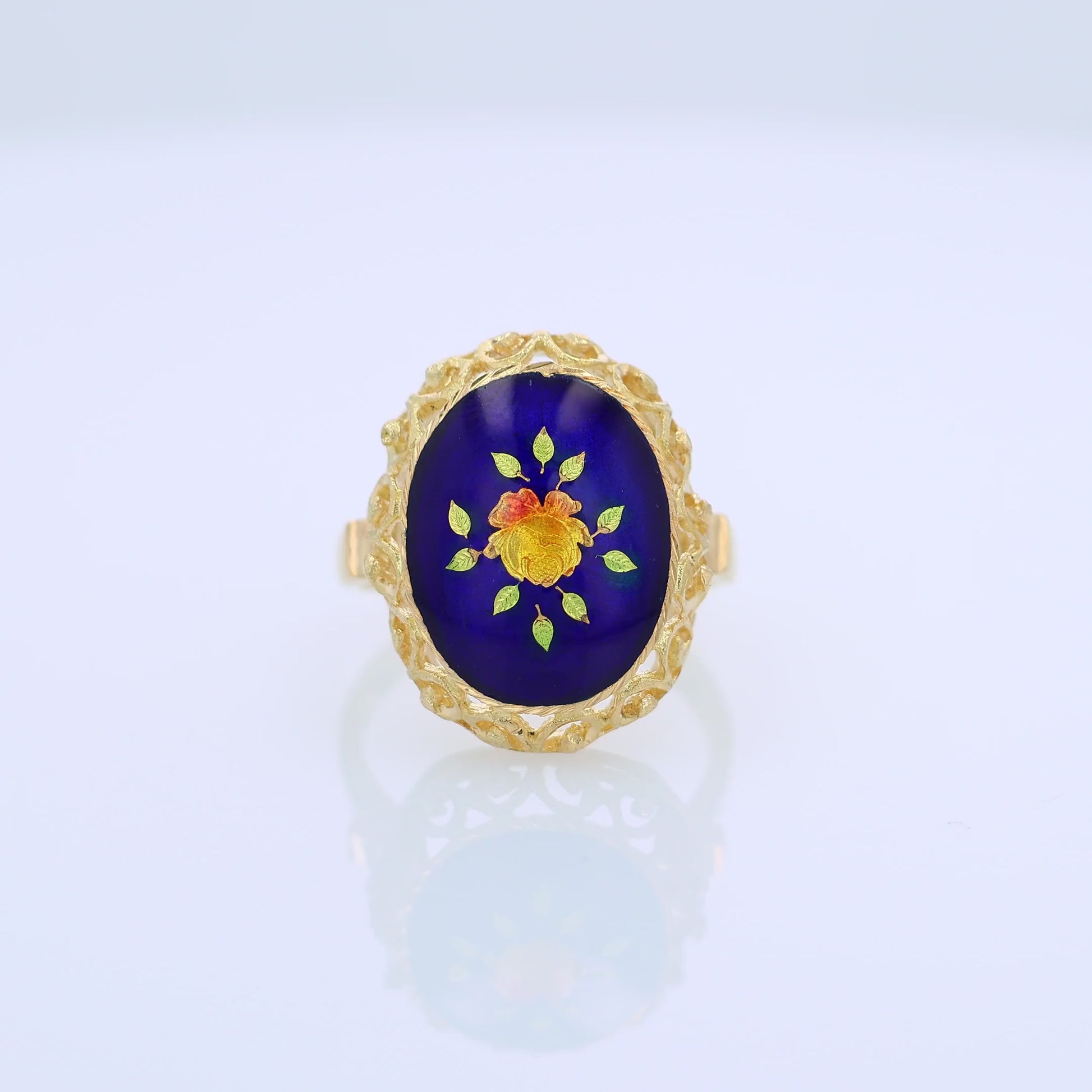 360 degree video of a yellow gold ring with a blue, orange and green flower design enamel center on a white background