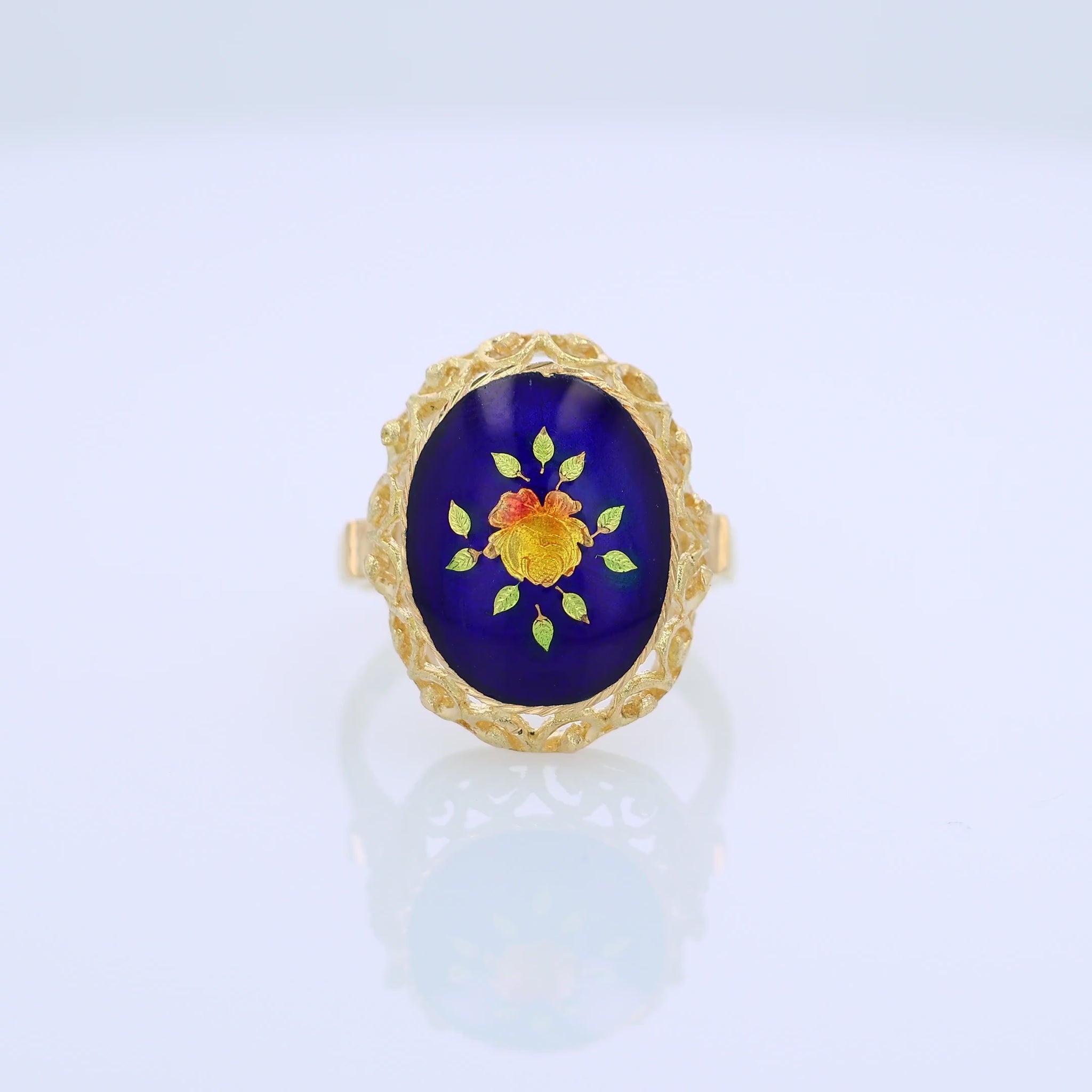 360 degree video of a yellow gold ring with a blue, orange and green flower design enamel center on a white background