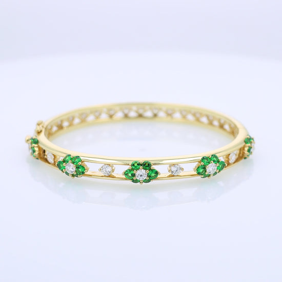 Yellow gold bracelet with green tsavorites and diamond accents on a white background