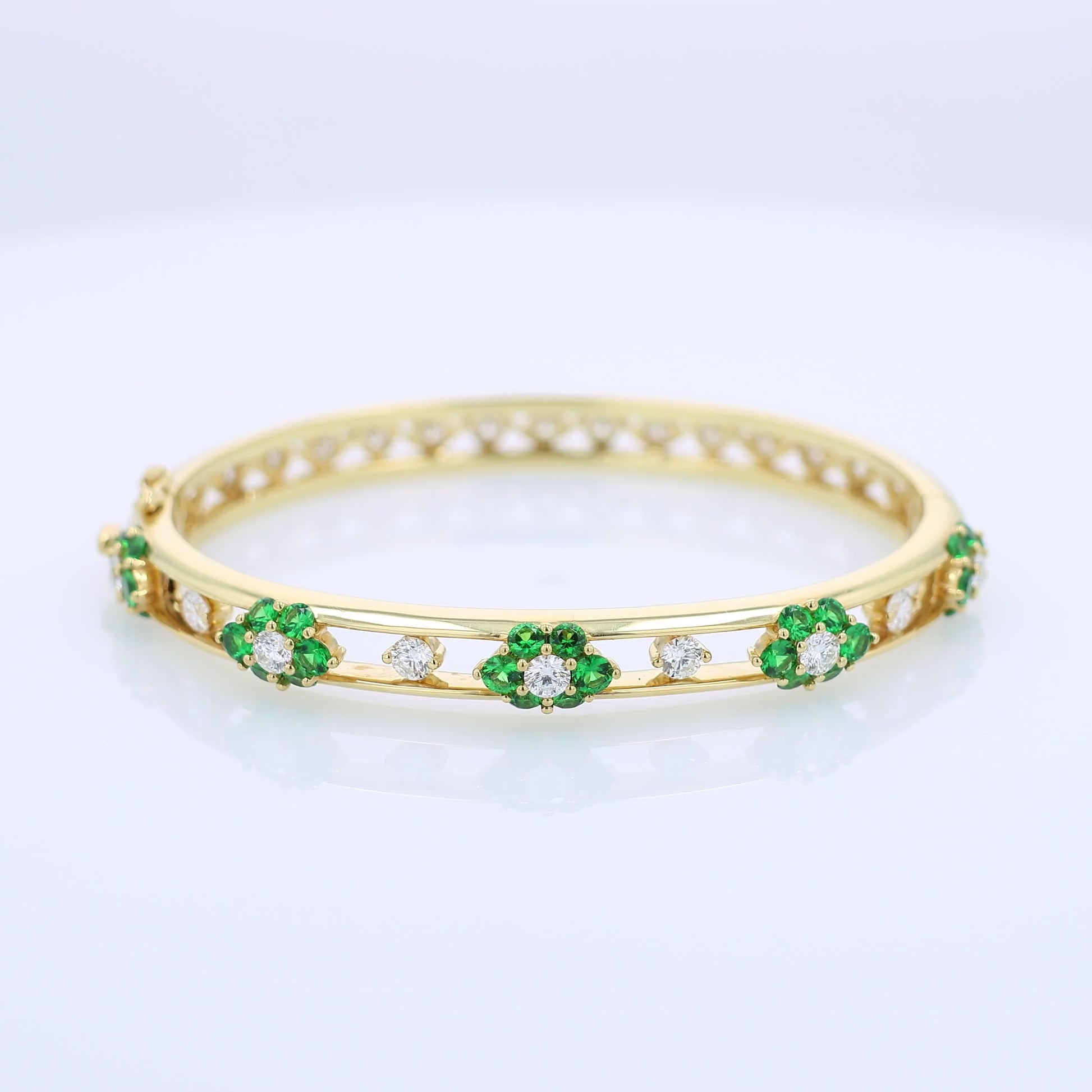 Yellow gold bracelet with green tsavorites and diamond accents on a white background