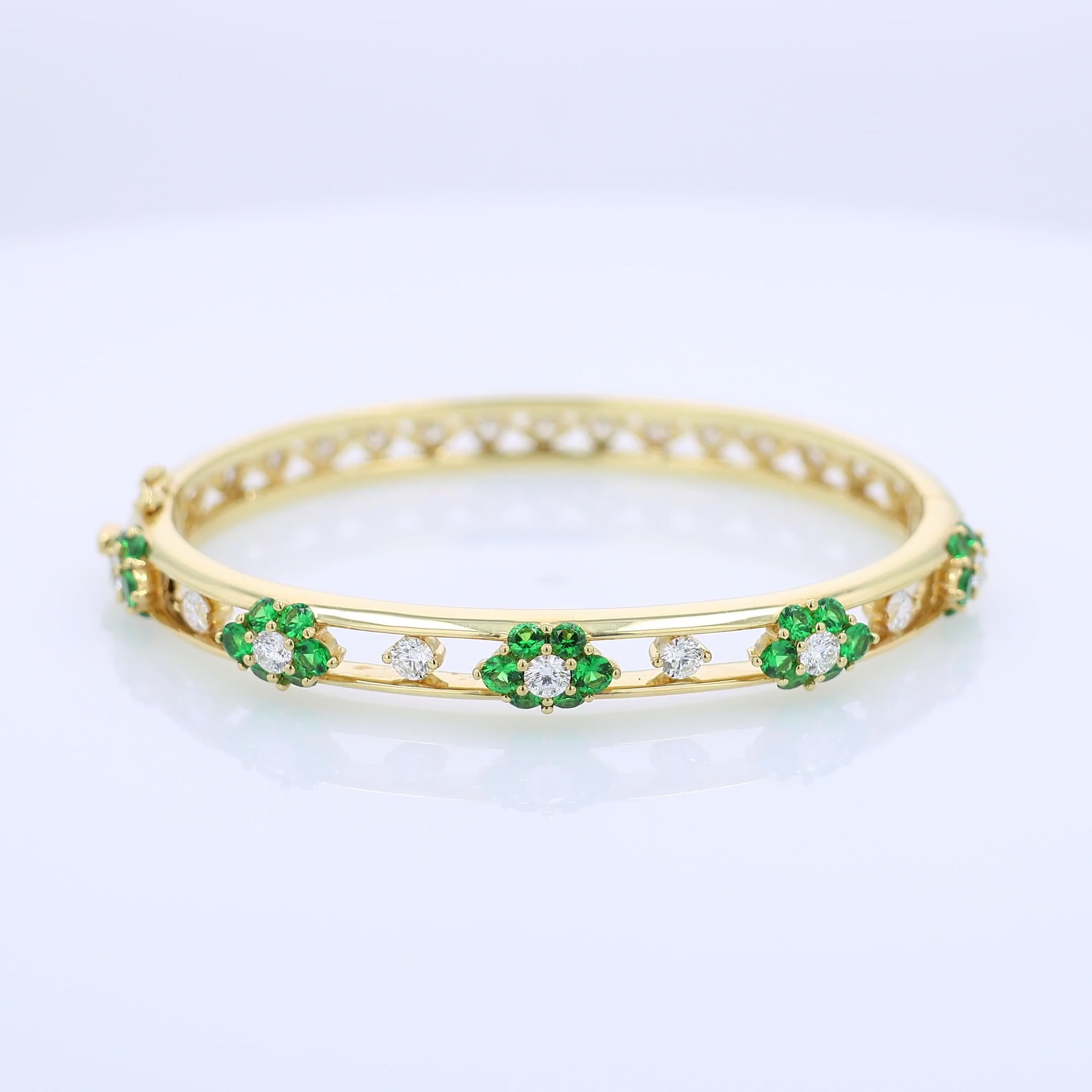 Yellow gold bracelet with green tsavorites and diamond accents on a white background