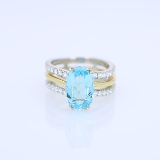 Two-tone ring with an oval swiss blue topaz center and diamond accents on a white background