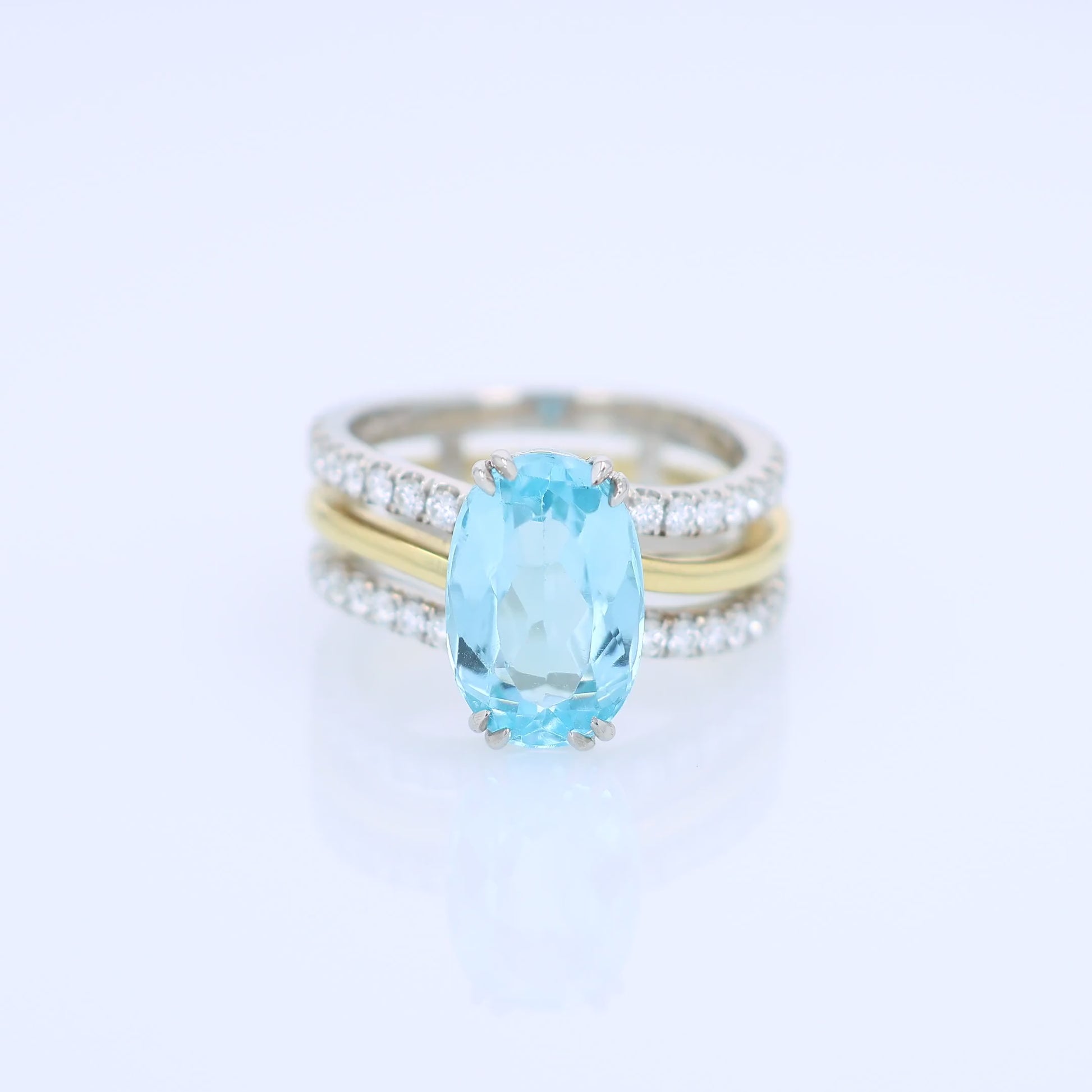 Two-tone ring with an oval swiss blue topaz center and diamond accents on a white background