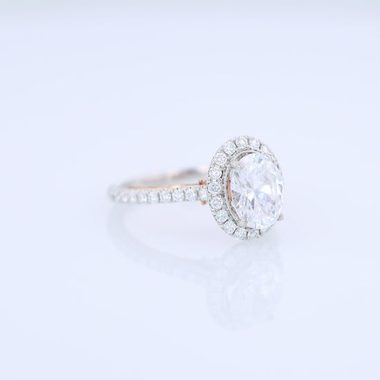 White and rose gold and diamond halo engagement ring with diamond accents and an oval cubic zirconia center on a white background