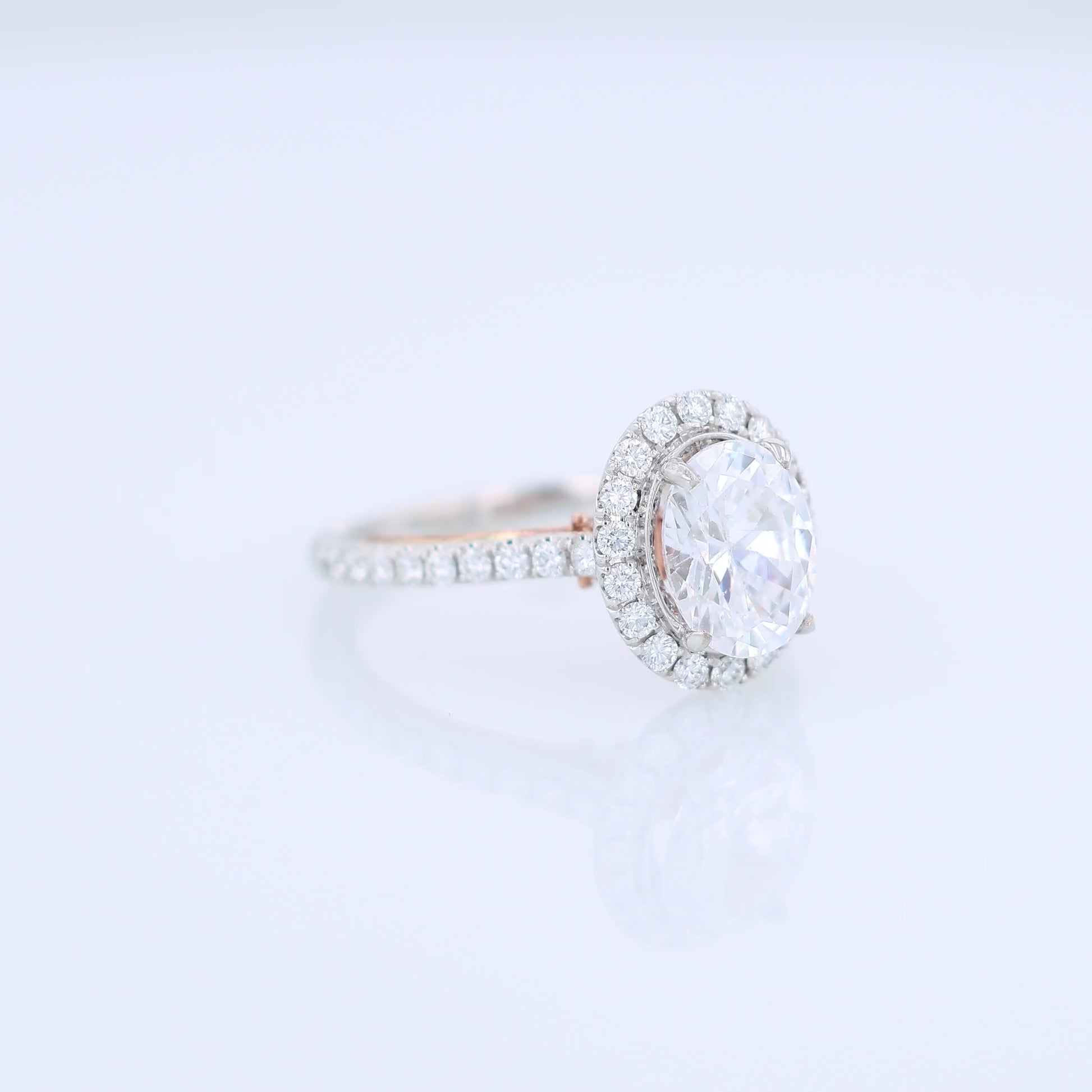 White and rose gold and diamond halo engagement ring with diamond accents and an oval cubic zirconia center on a white background