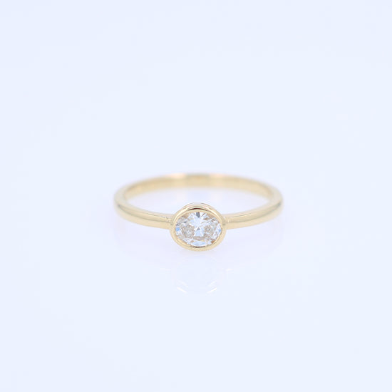 A delicate yellow gold ring featuring a bezel-set oval diamond, shown against a plain white background.