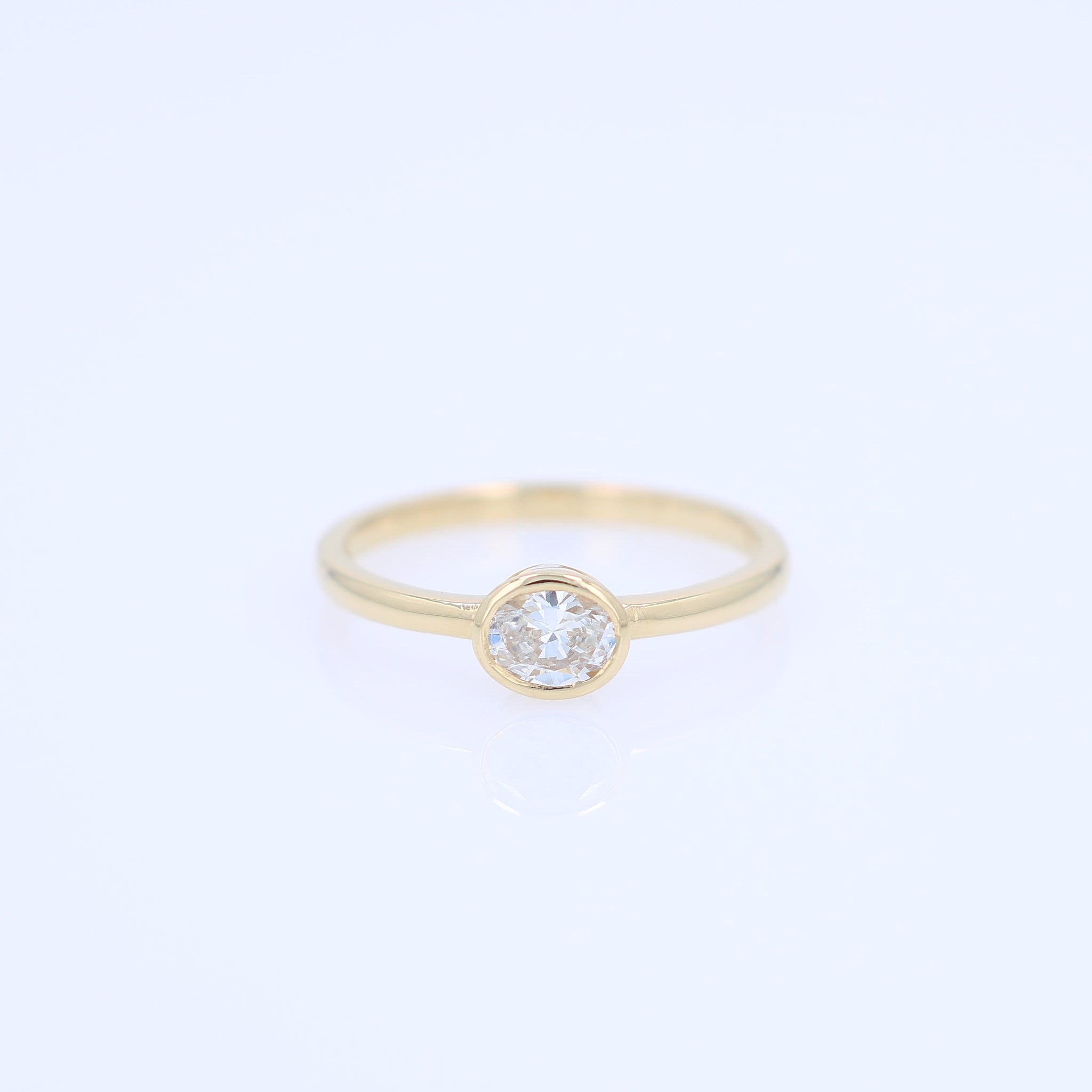 A delicate yellow gold ring featuring a bezel-set oval diamond, shown against a plain white background.