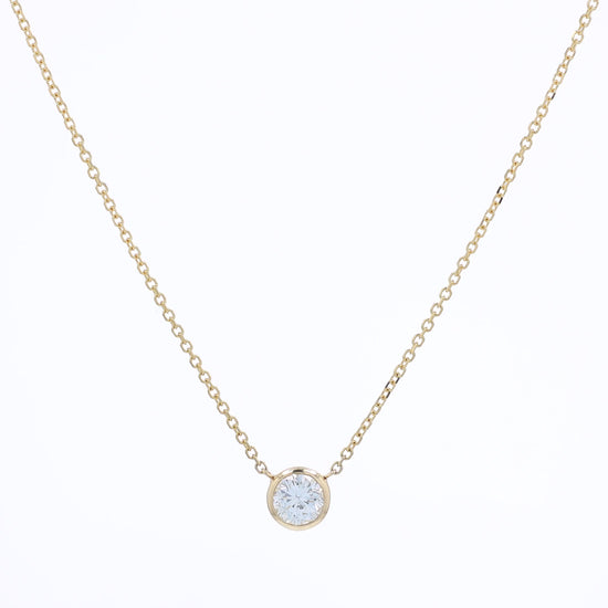 A delicate gold chain necklace with a small bezel-set pendant holding a clear round-cut diamond, displayed against a solid white background.