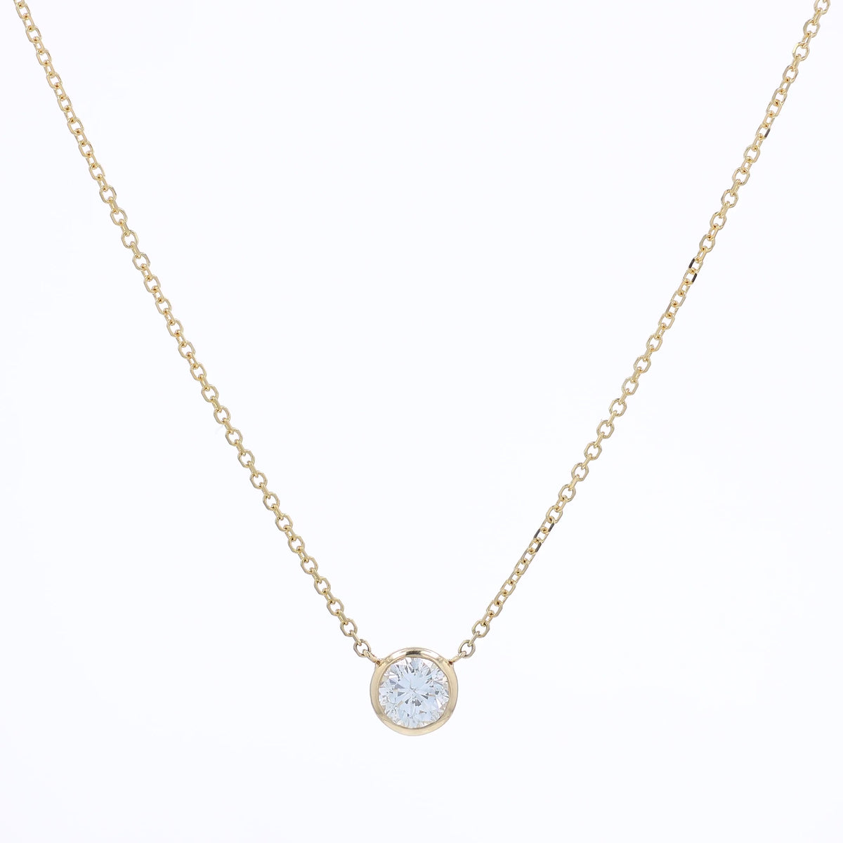 A delicate gold chain necklace with a small bezel-set pendant holding a clear round-cut diamond, displayed against a solid white background.