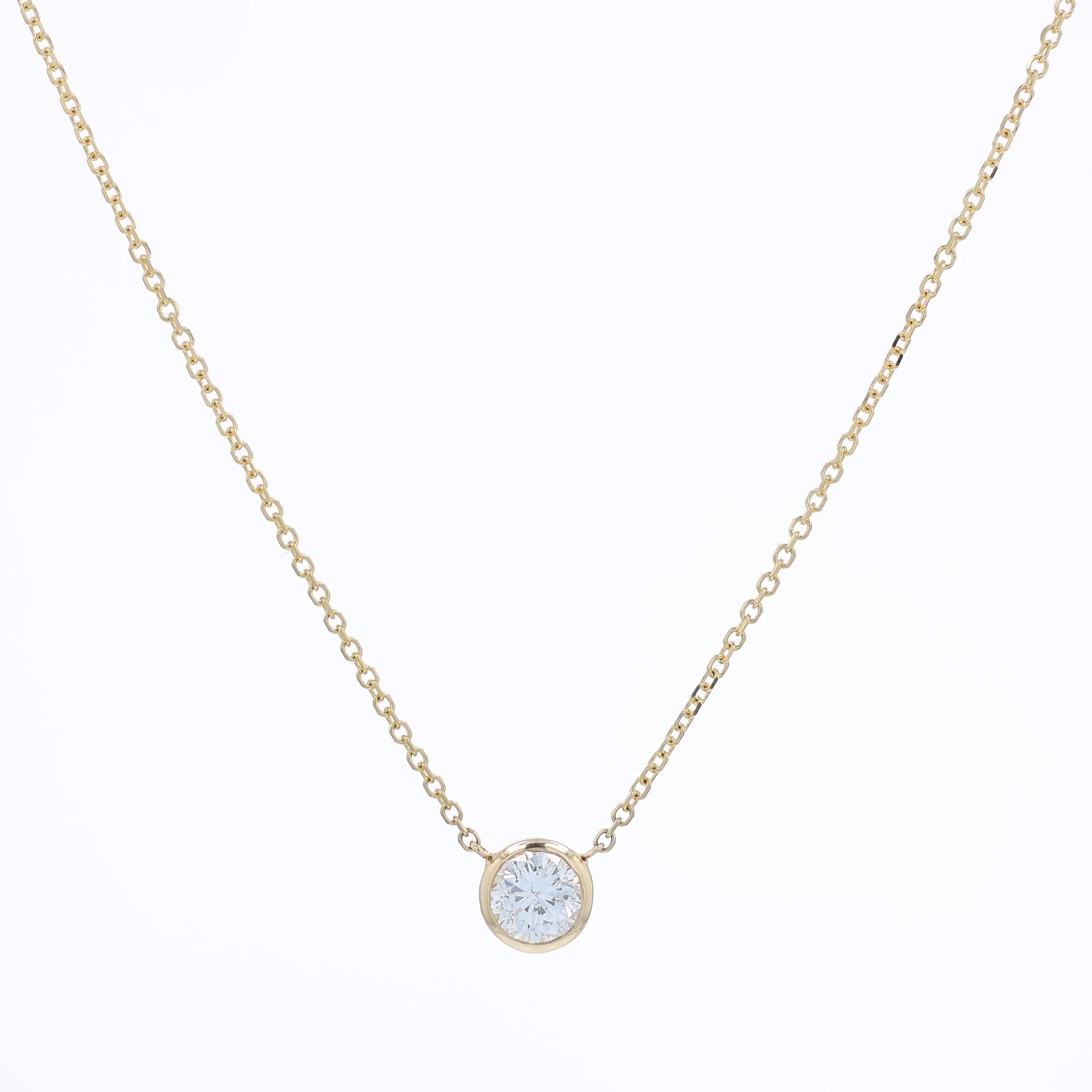 A delicate gold chain necklace with a small bezel-set pendant holding a clear round-cut diamond, displayed against a solid white background.
