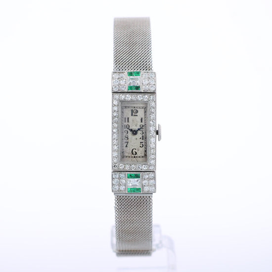 Estate platinum and white gold watch with diamond and emerald accents on case front with an off white dial on a white background