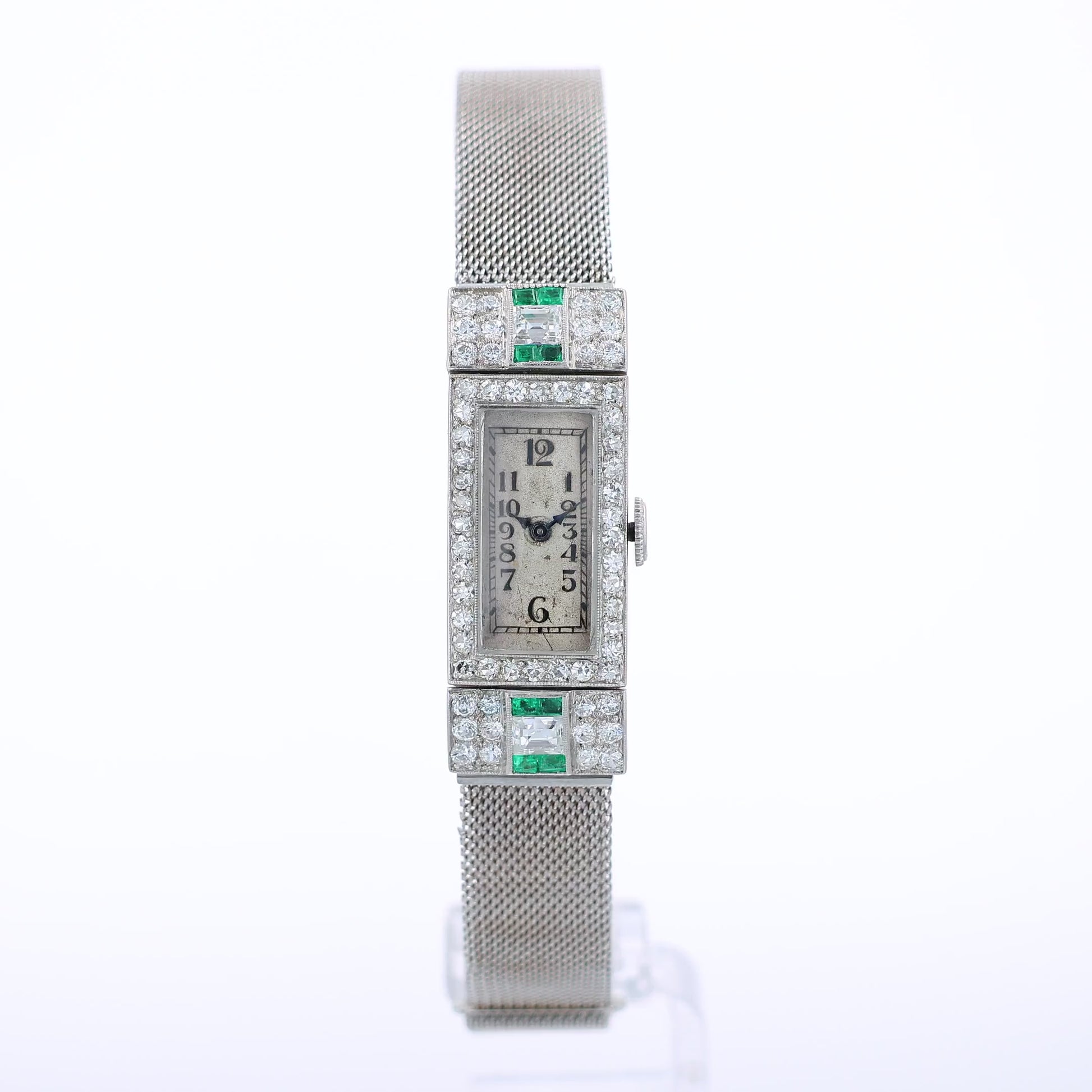Estate platinum and white gold watch with diamond and emerald accents on case front with an off white dial on a white background