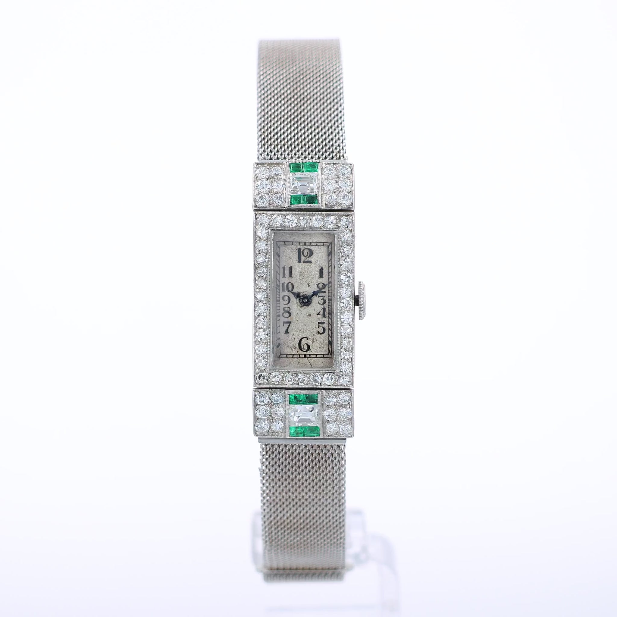 Estate platinum and white gold watch with diamond and emerald accents on case front with an off white dial on a white background