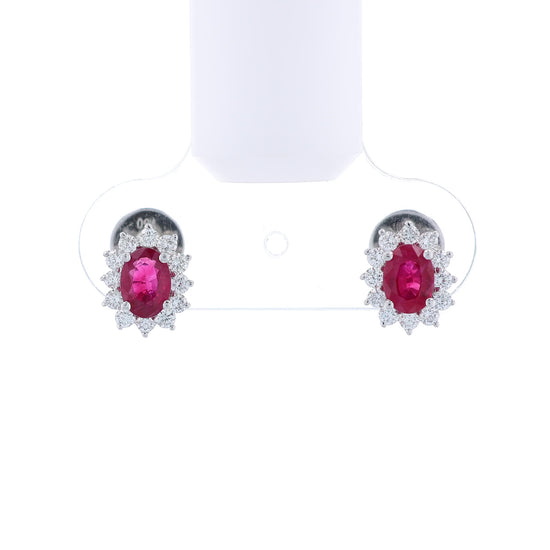 Pair of white gold diamond halo earrings with oval ruby centers on a white background