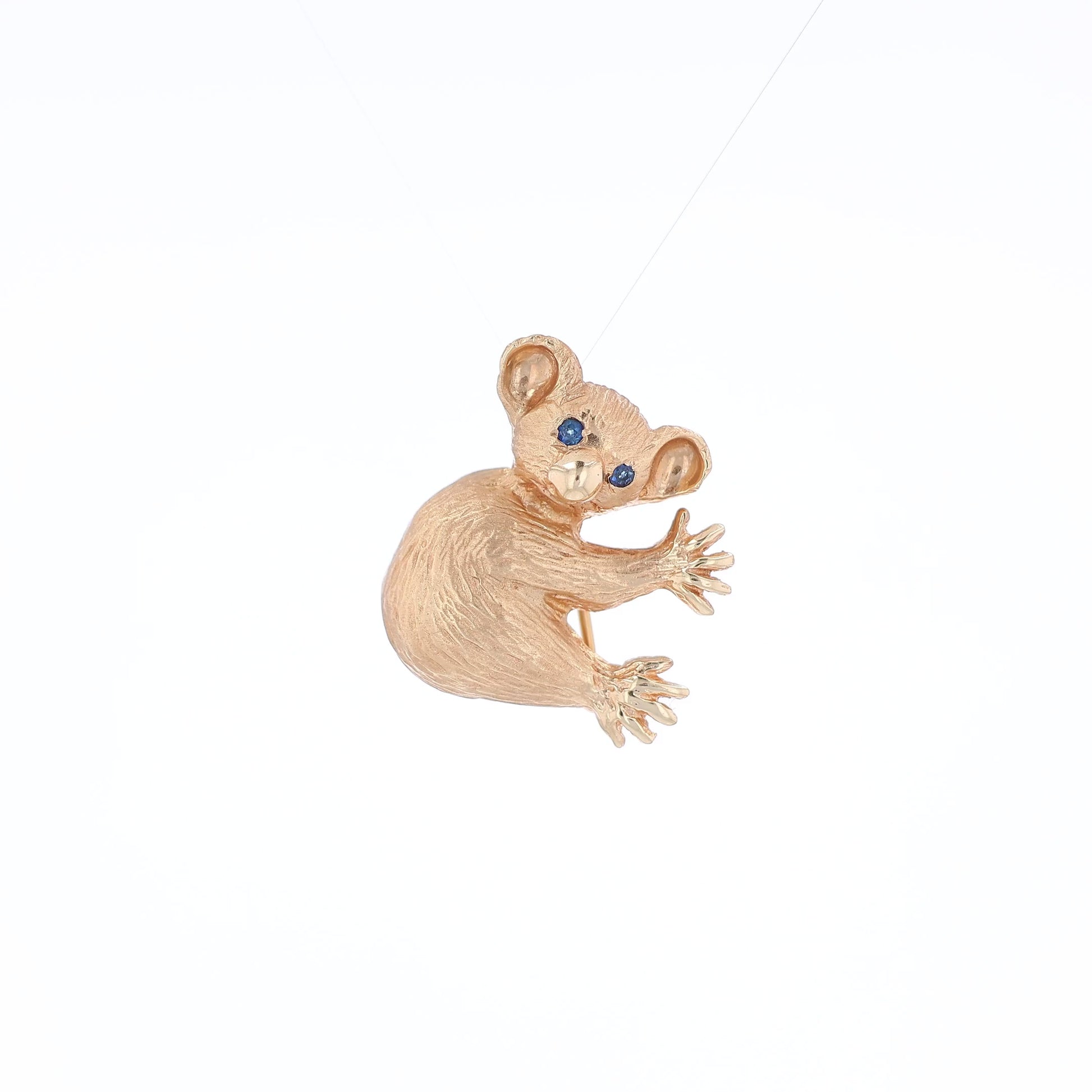 Yellow gold brushed koala pin with two round blue sapphire eyes on a white background