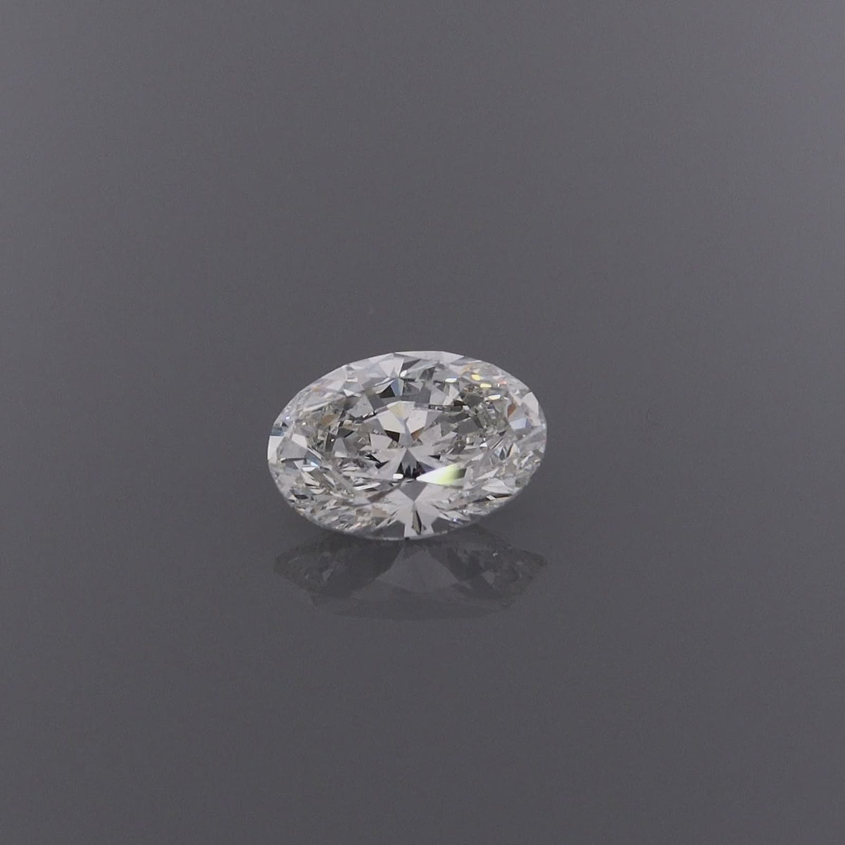 A video of an oval-cut diamond gemstone with a brilliant faceted cut, on a clean grey background with a subtle reflection below.