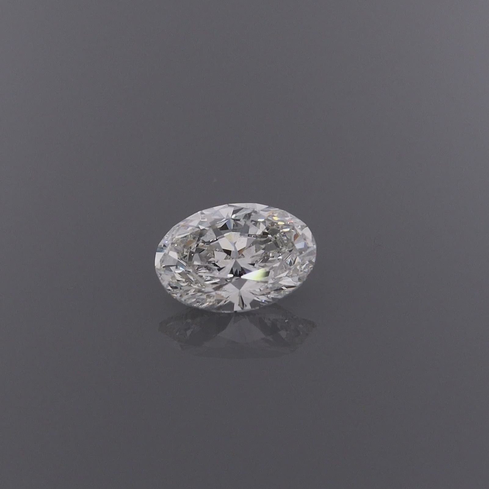 A video of an oval-cut diamond gemstone with a brilliant faceted cut, on a clean grey background with a subtle reflection below.