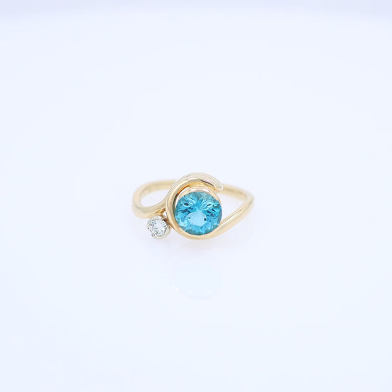 Yellow gold bezel set blue topaz and diamond ring on a white background