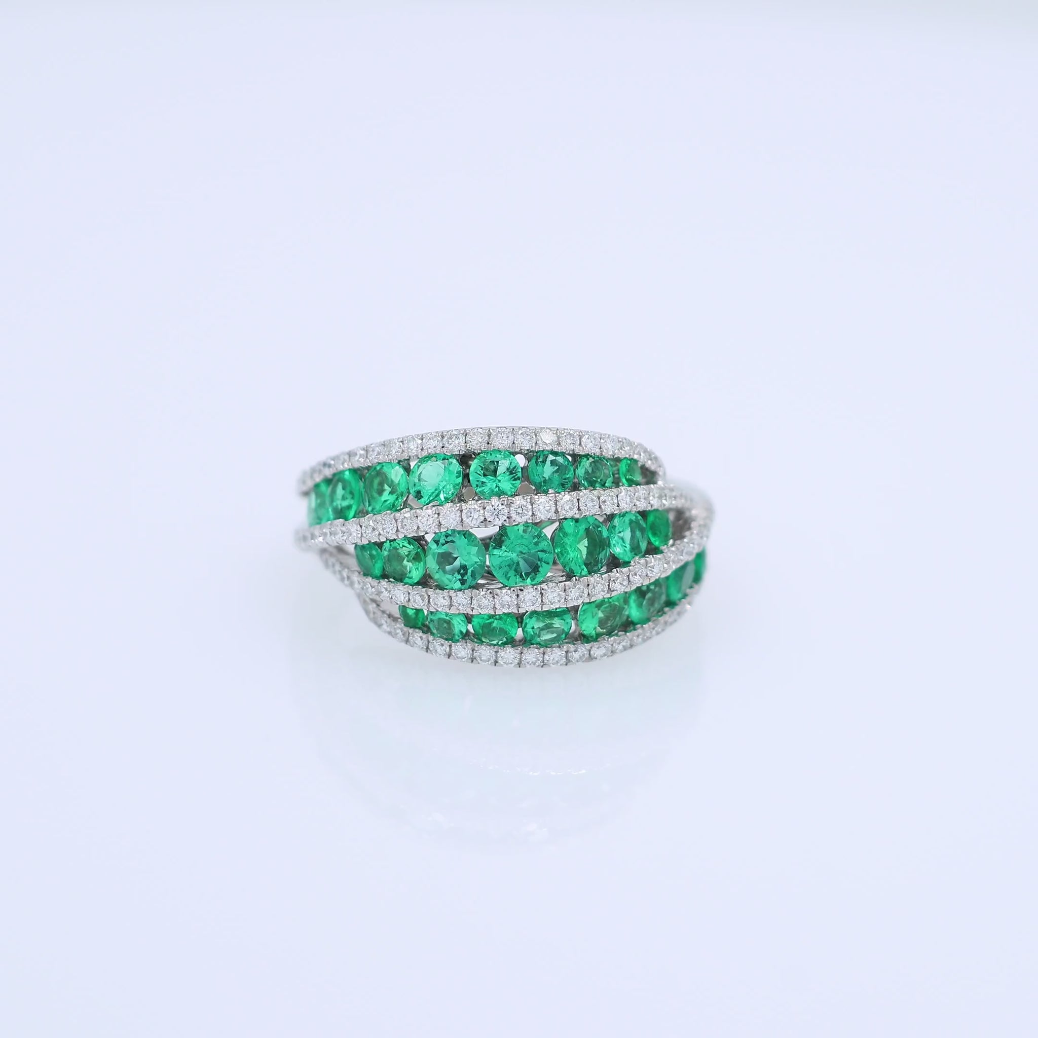 White gold multi-row graduated emerald and diamond ring on a white background