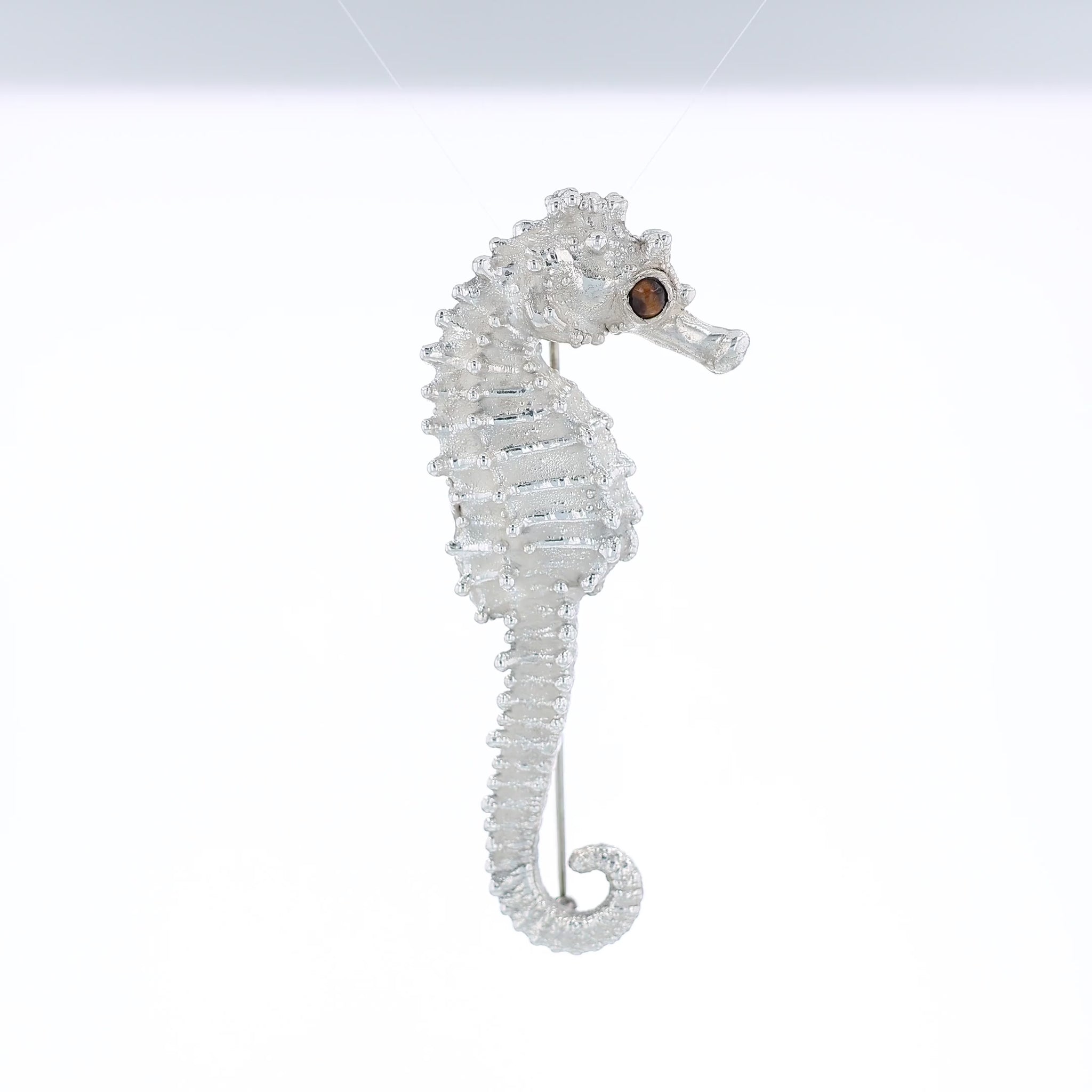 Sterling silver seahorse pin with a round tiger's eye in the eye on a white background