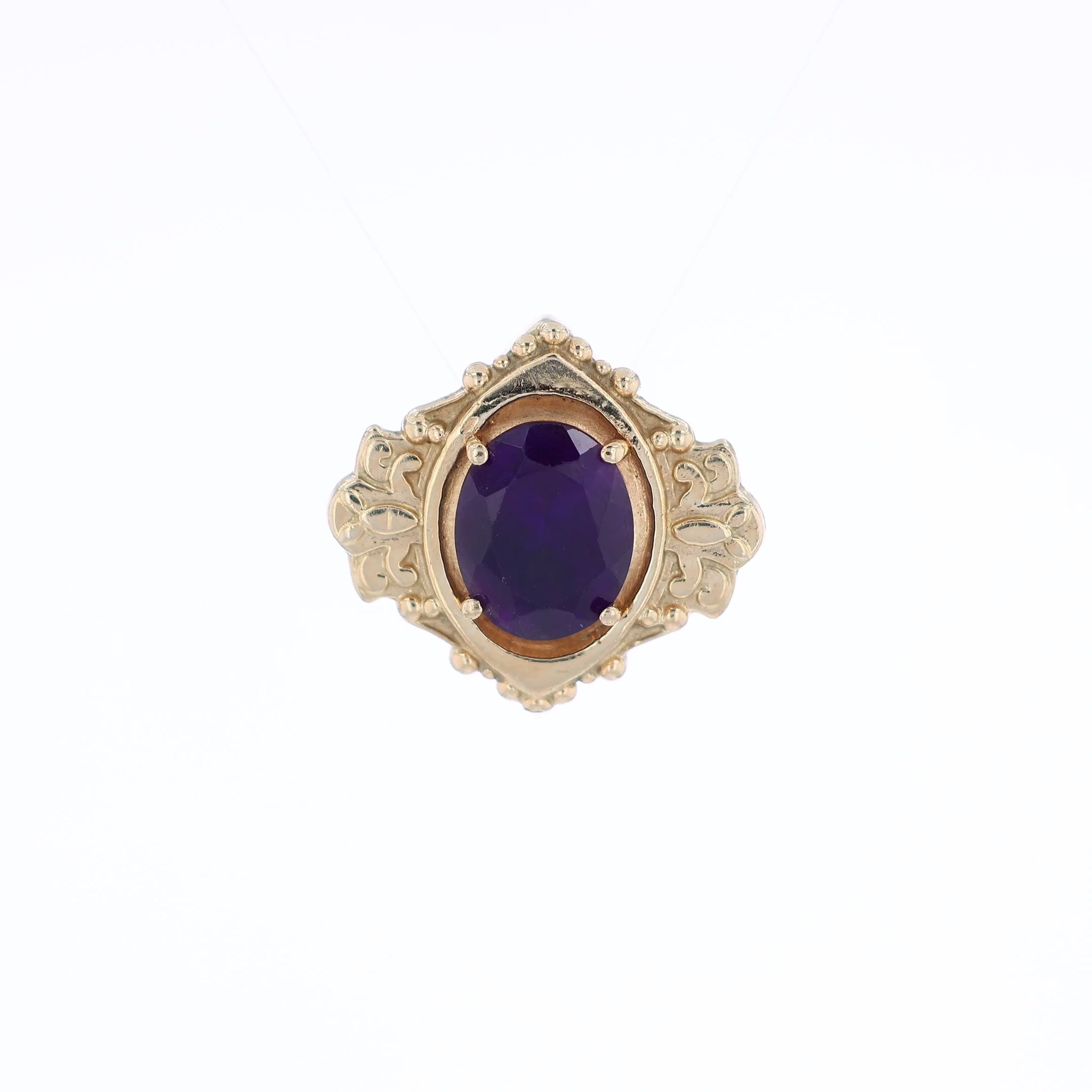 Yellow gold oval amethyst slide pendant with an ornate shield shaped frame on a white background