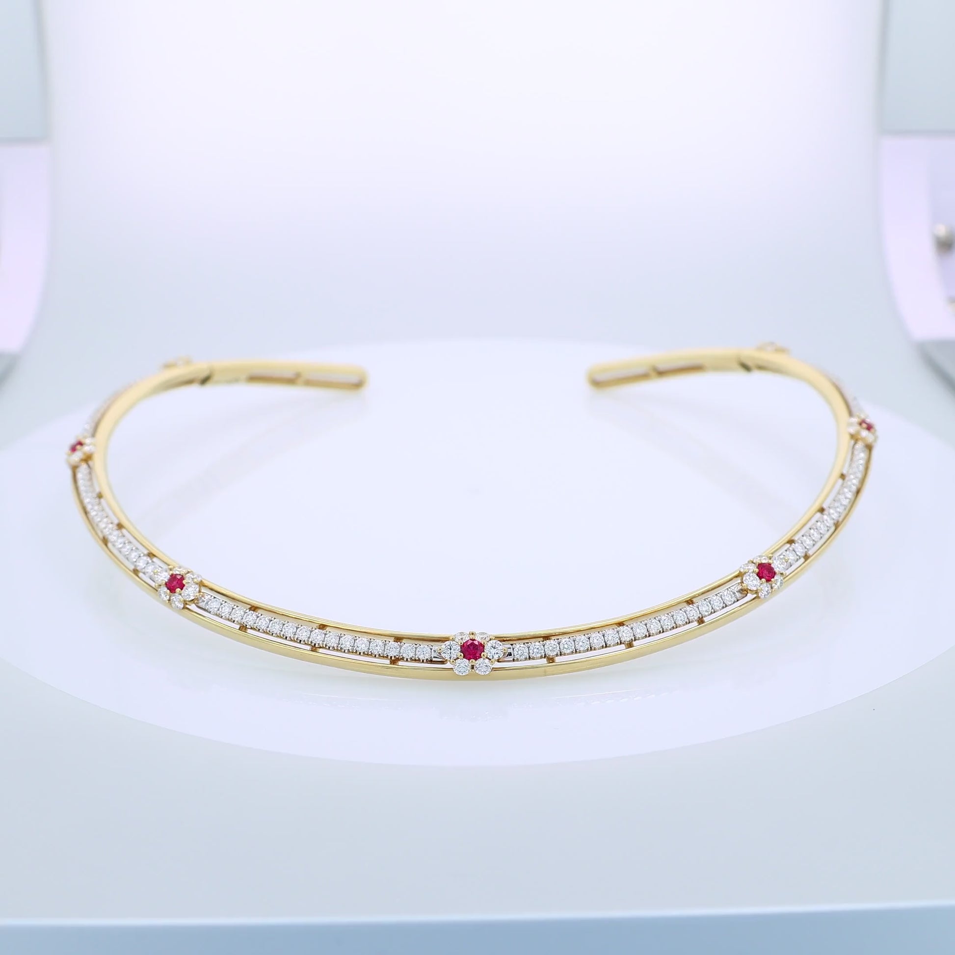 Gold collar necklace with diamond center row and ruby accents on a white background
