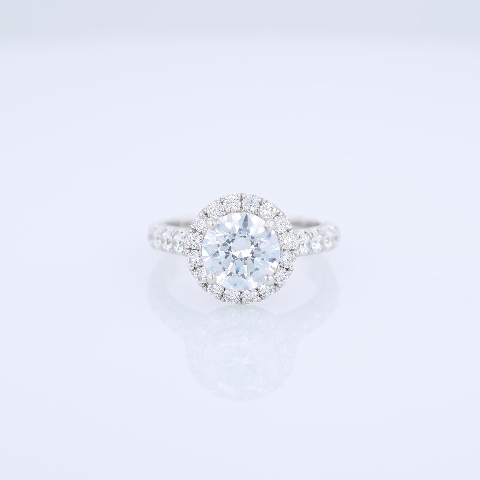 White gold diamond halo engagement ring with diamond accents and a round cubic zirconia center on a white background