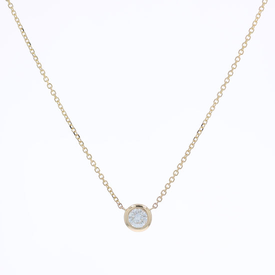 A delicate gold chain necklace with a small bezel-set pendant holding a clear round-cut diamond, displayed against a solid white background.