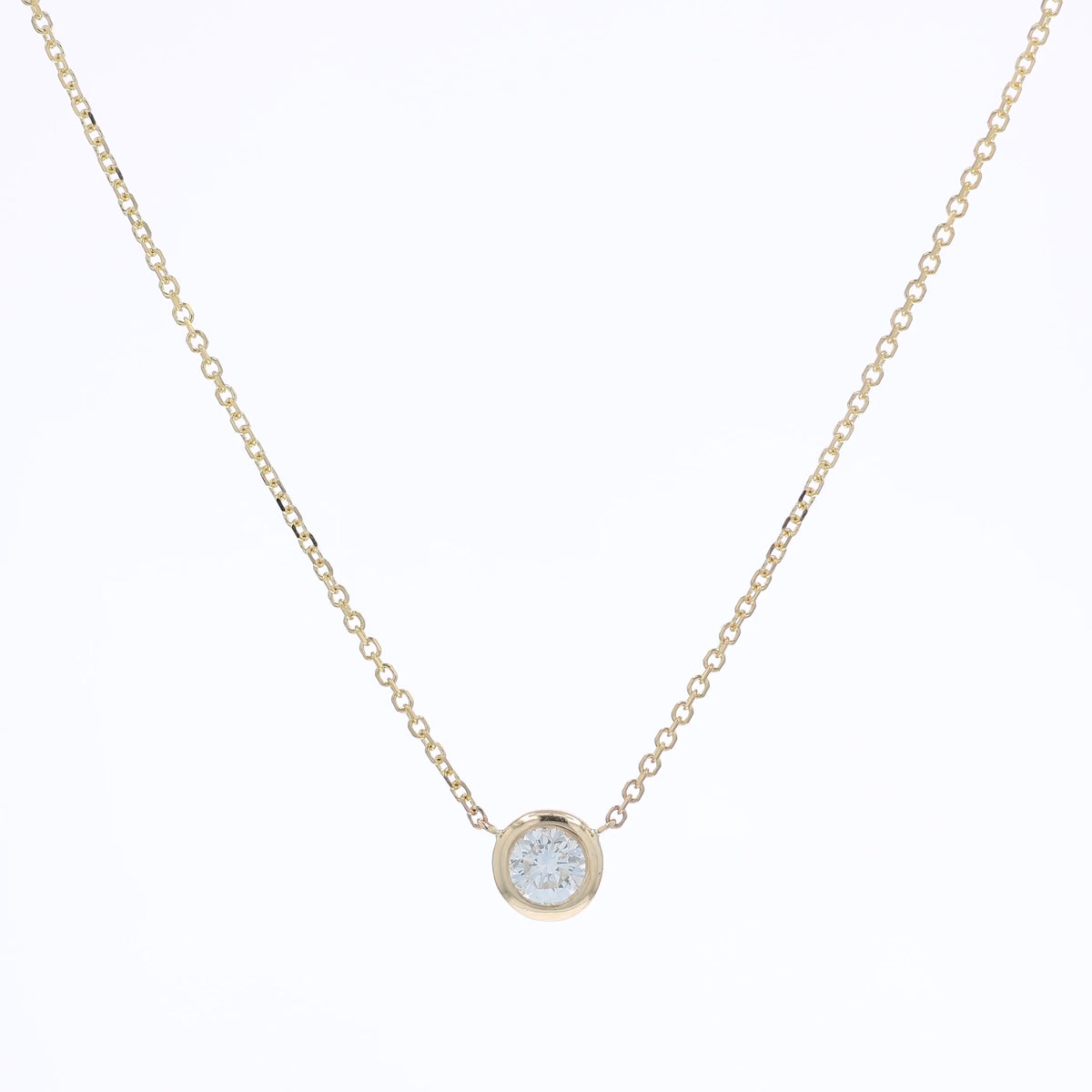A delicate gold chain necklace with a small bezel-set pendant holding a clear round-cut diamond, displayed against a solid white background.